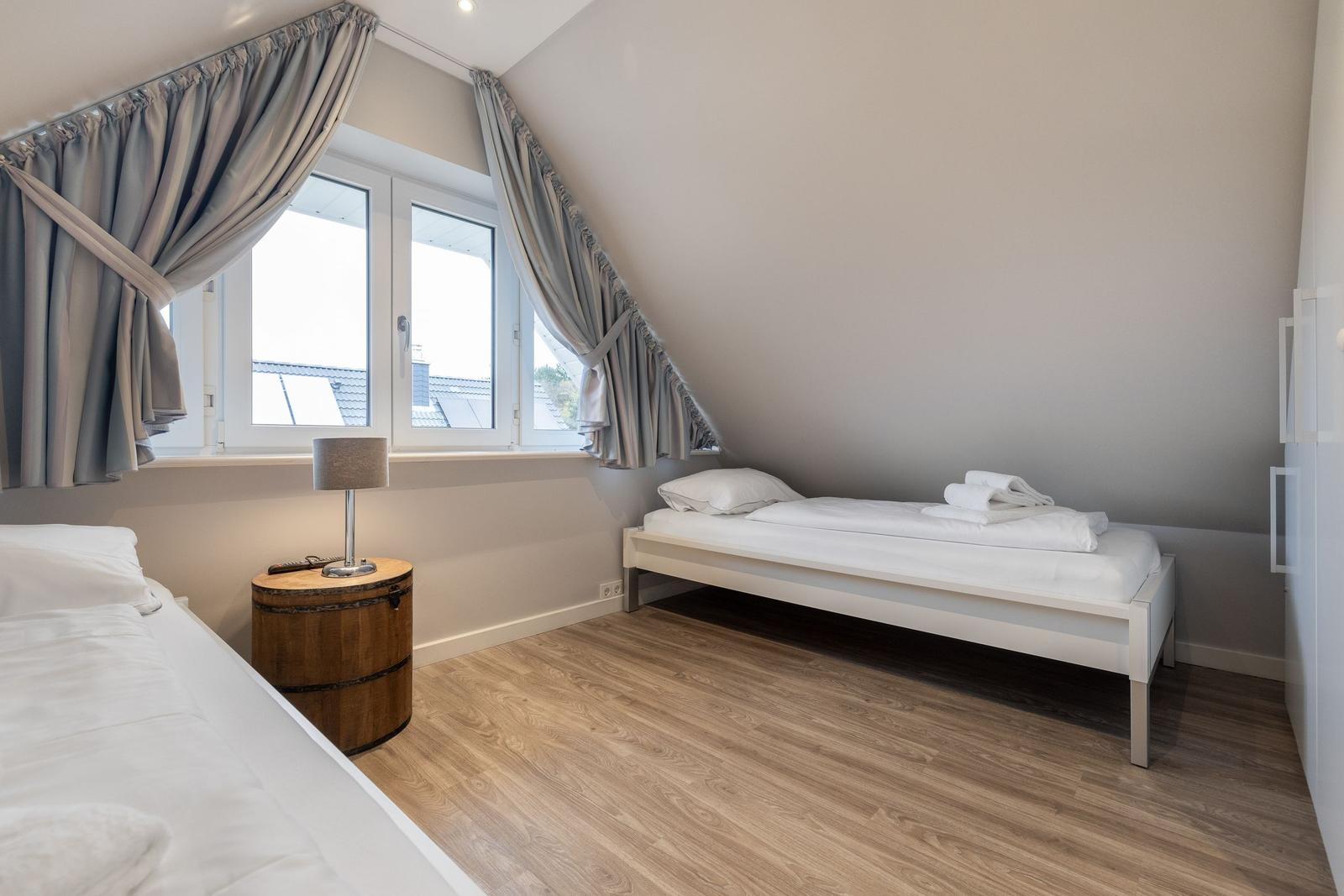 Room with two beds, wooden floor, and large window with curtains.