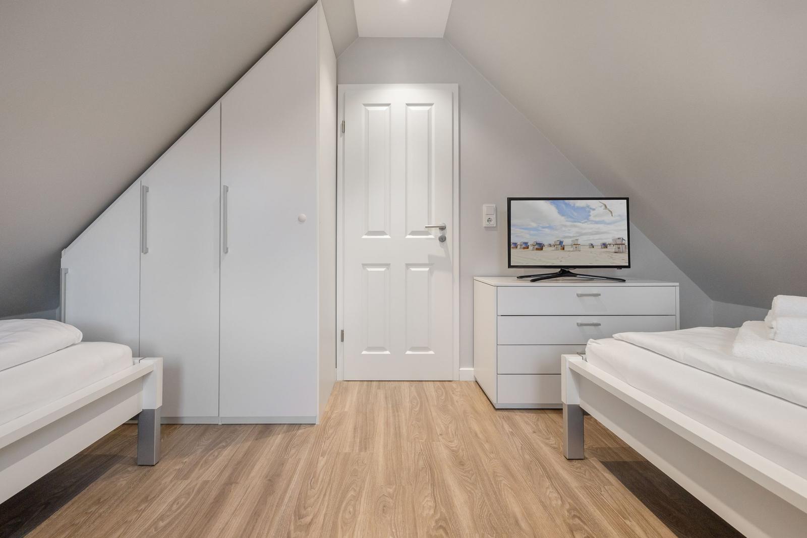 Room with two beds, wardrobe, and TV on dresser.