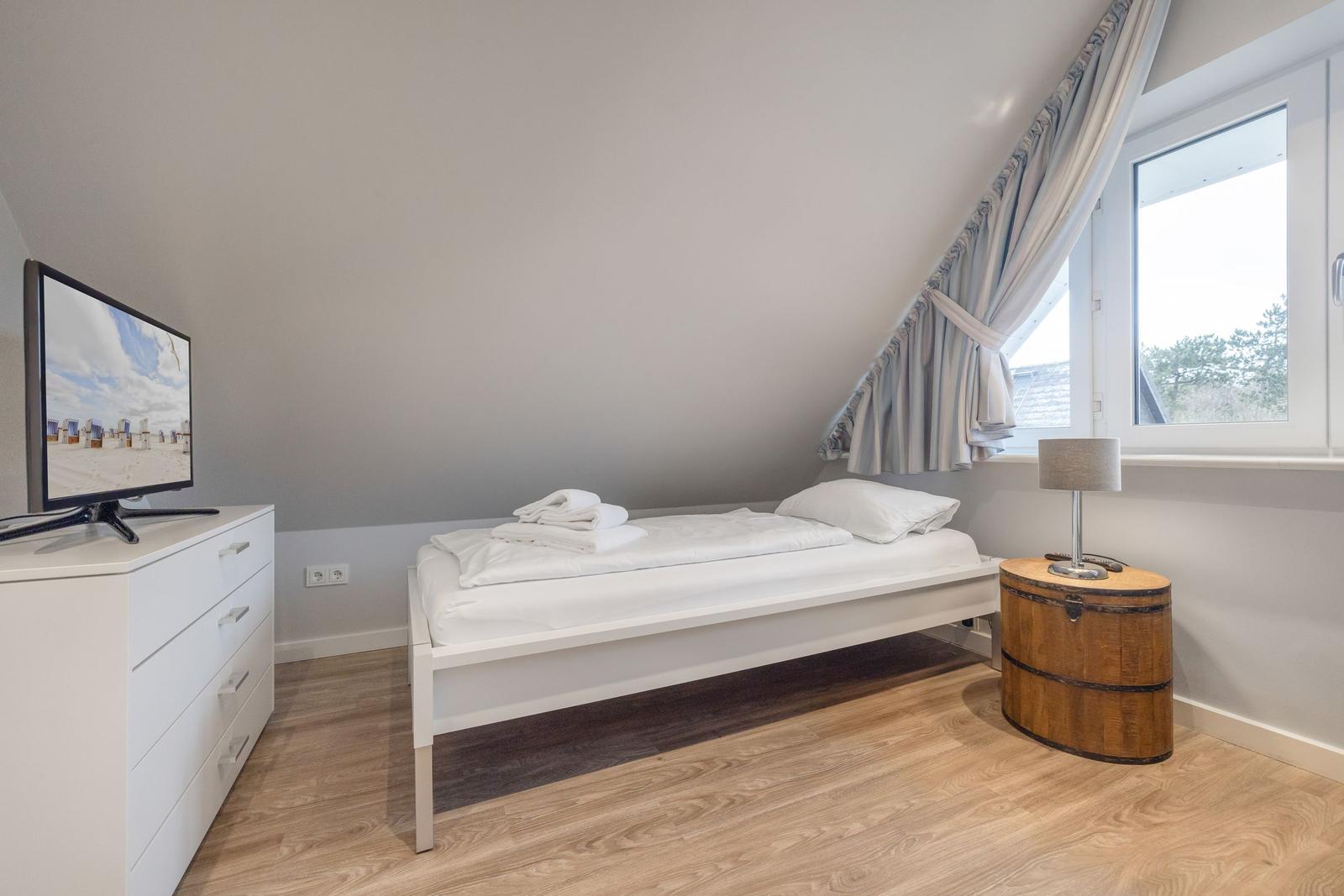 Bedroom with bed, TV, and window. Wooden floor and wooden barrel nightstand.