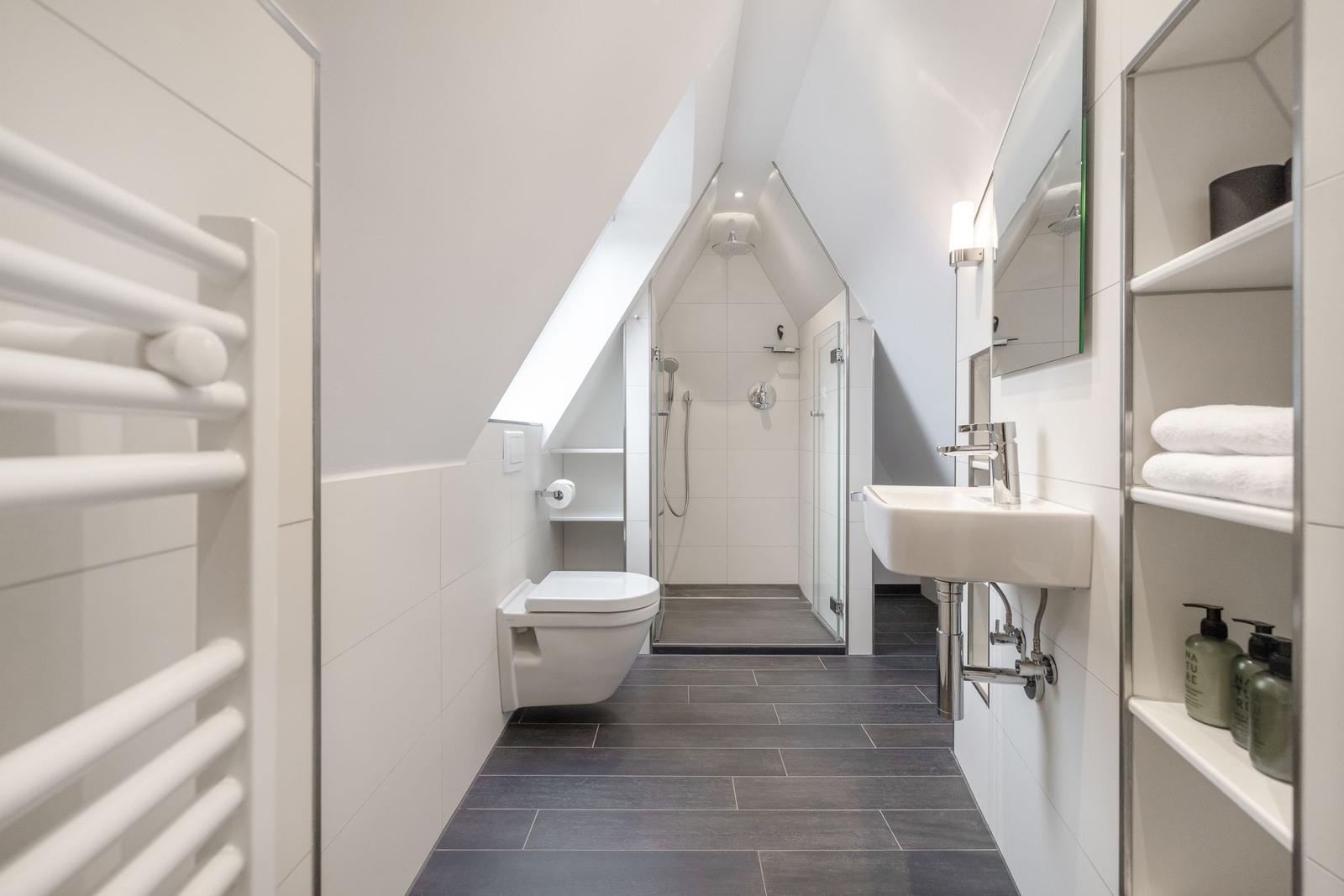 Bathroom with shower, sink, and toilet under sloped ceiling.