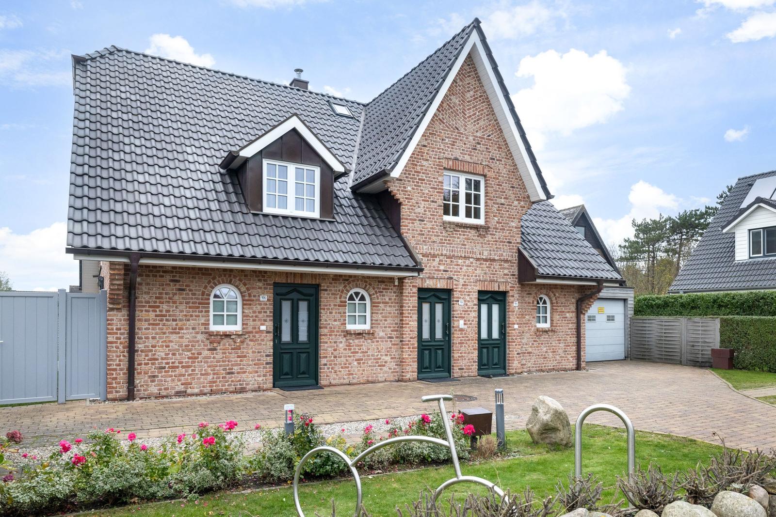 A two-story house with brick facade and gray roof. Front garden with flowers and bike rack.