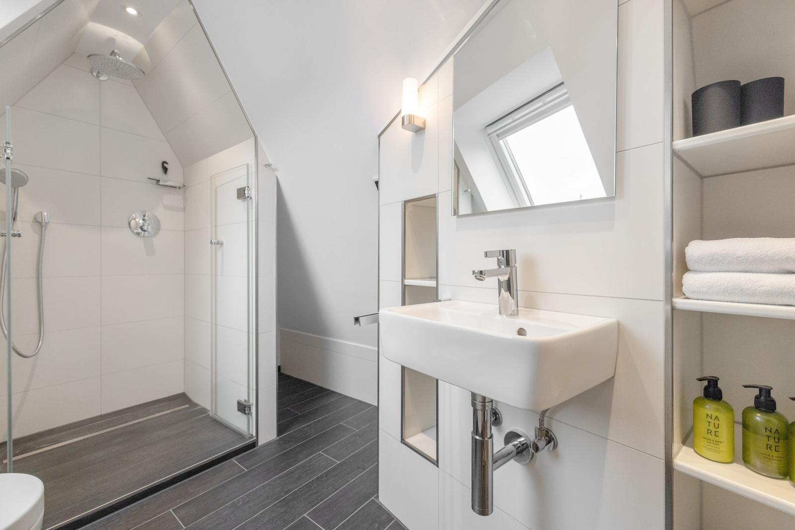 Bathroom with shower, sink, and shelves with towels and toiletries.