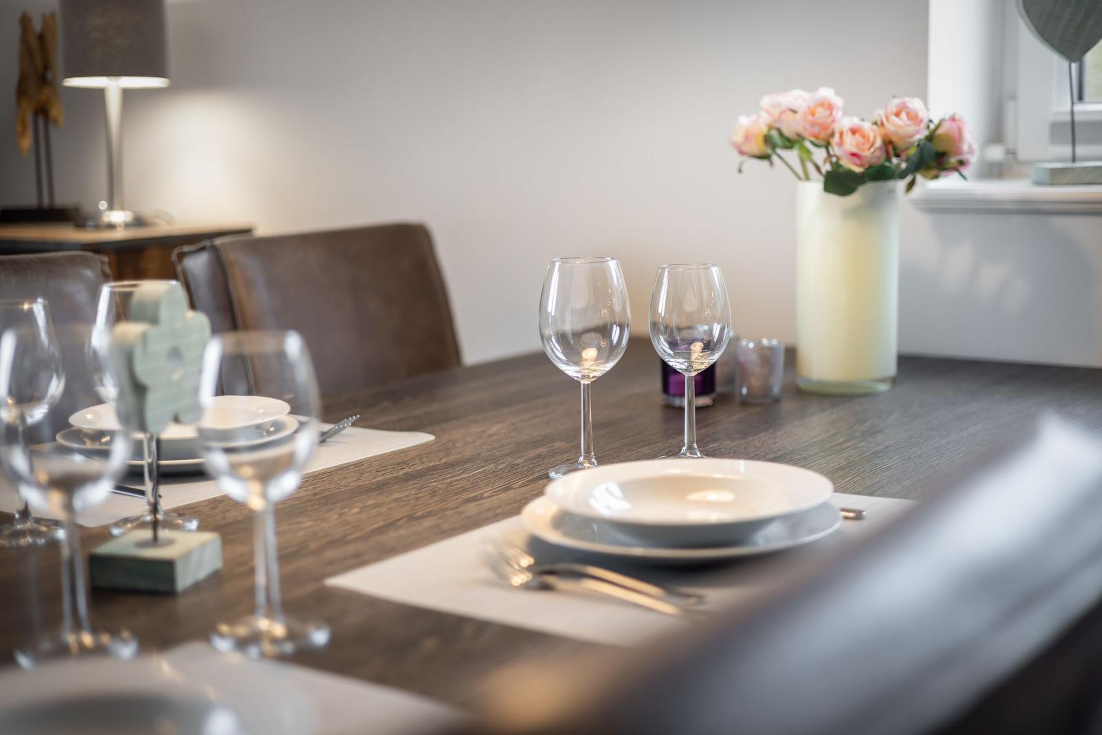 Set dining table with glasses, plates, and flowers in the background.