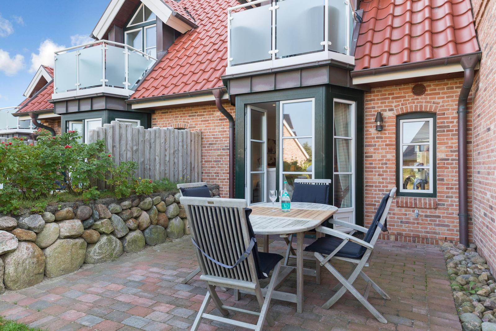 Terrace with table and chairs in front of a brick house with red roof.