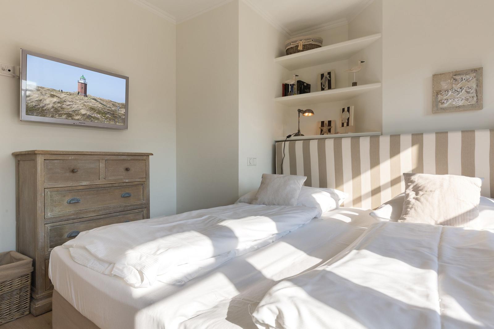 Bedroom with double bed, dresser, and wall picture. Shelf with decorative items.