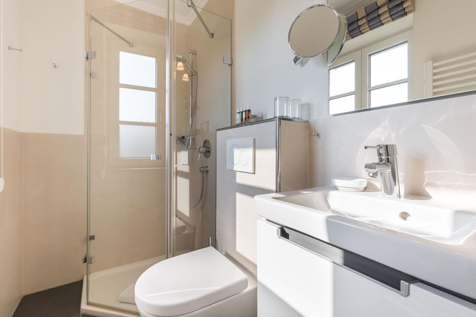 Bathroom with shower, sink, and toilet. Windows provide natural light.