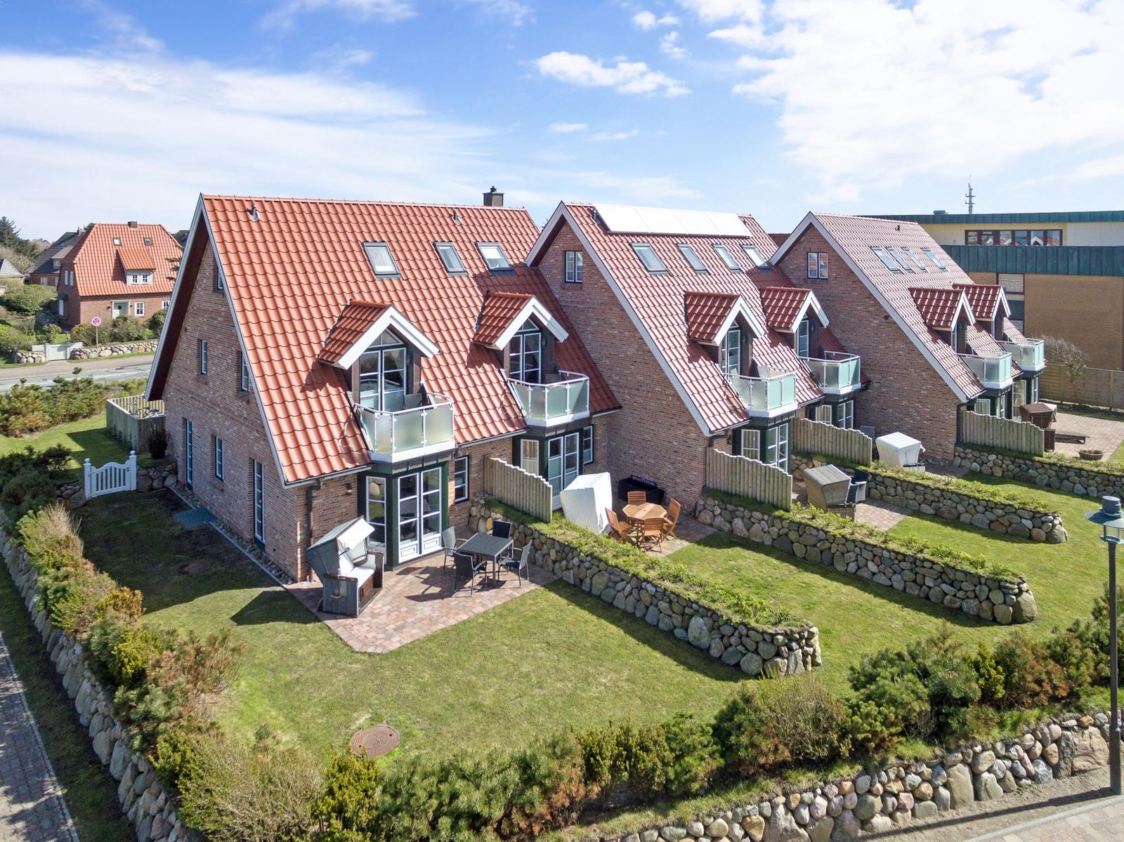 Holiday home with red roof and balconies, surrounded by lawns and stone walls.