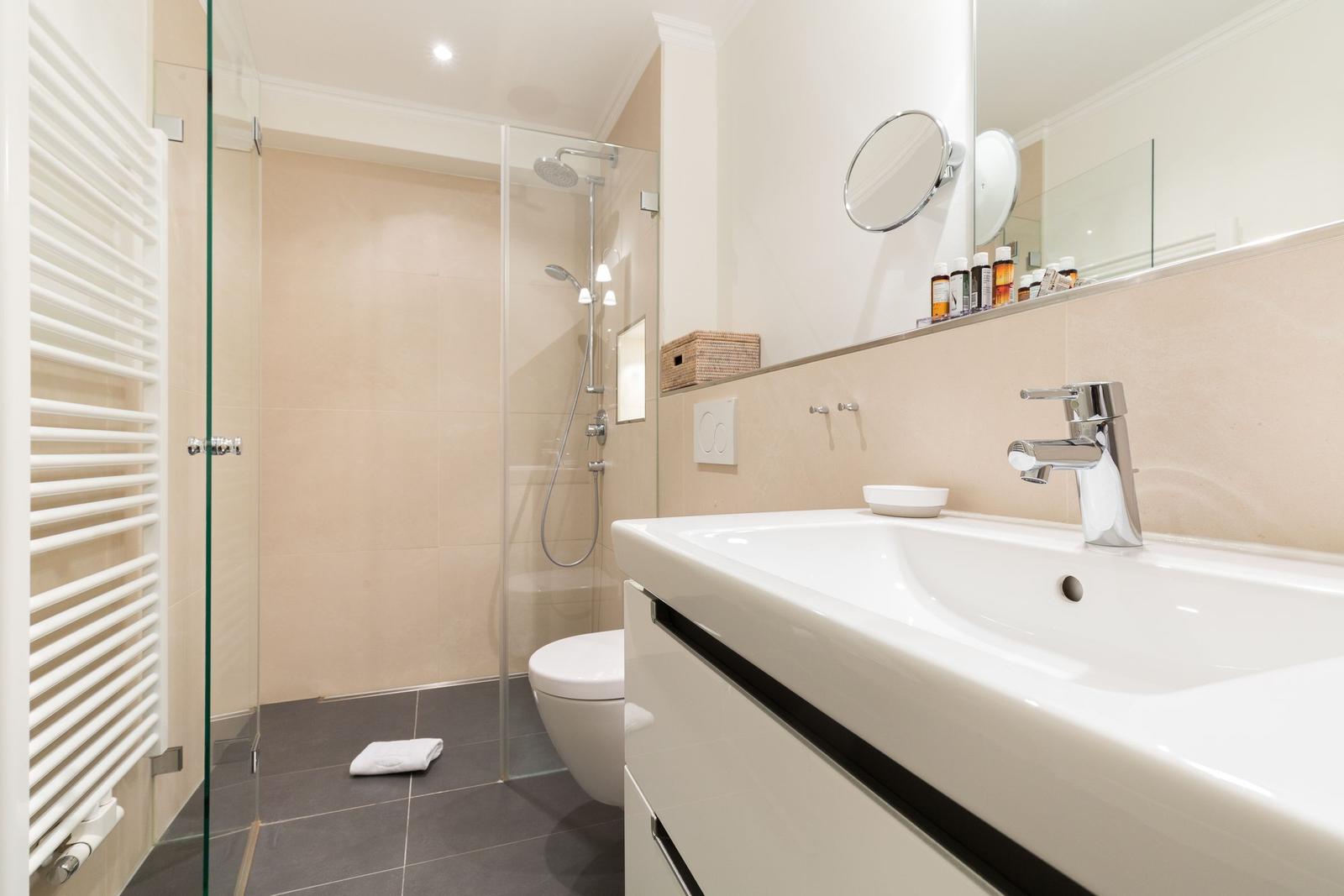Bathroom with shower, sink, and toilet. Mirror, towel, and tiles visible.