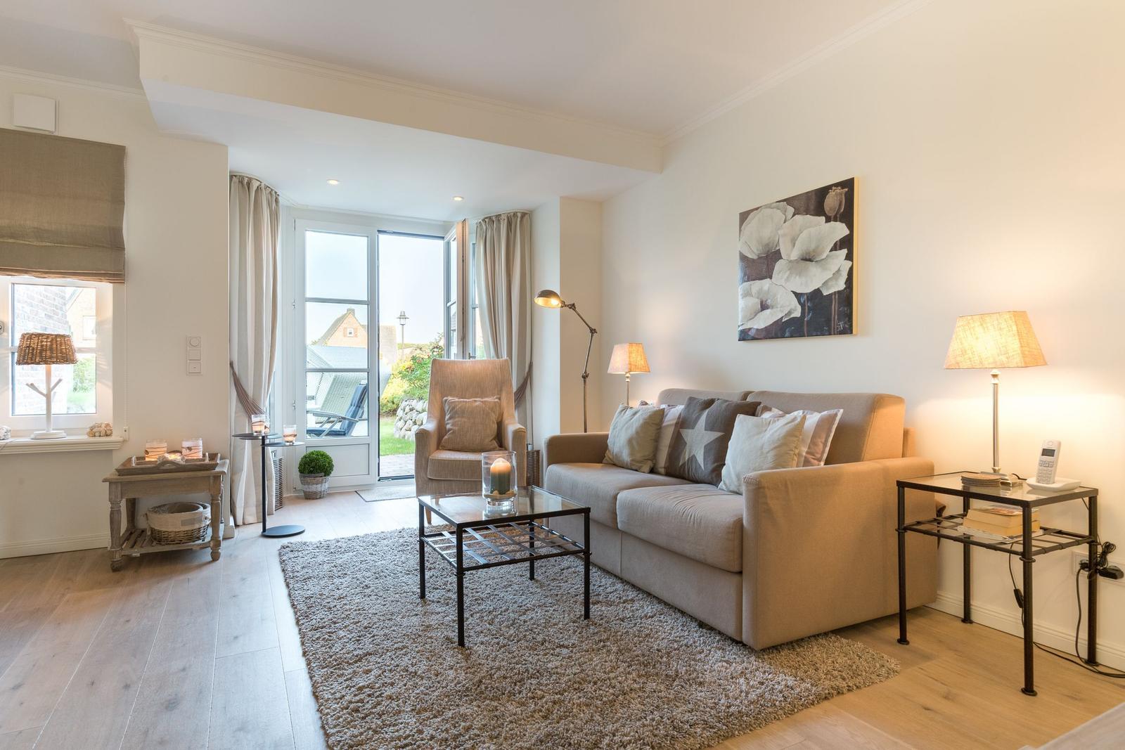 Living room with sofa, armchair, and glass table. Window to terrace. Wall art and lighting.