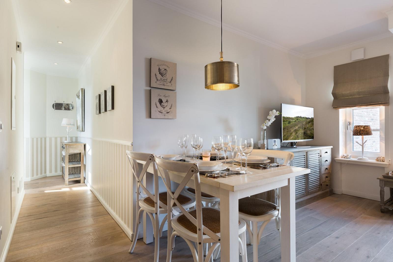 Dining room with table, chairs, and TV. Window with roller blind and wall art.