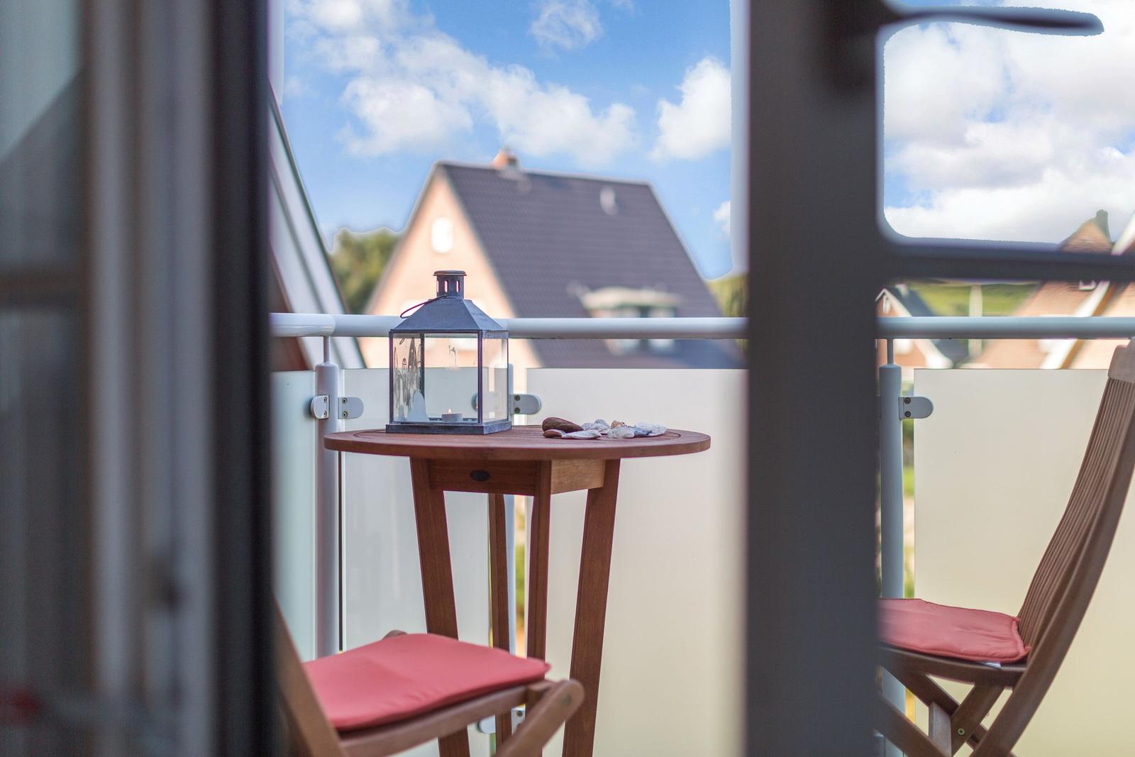 Balkon mit Tisch, Laterne und zwei Stühlen mit roten Sitzkissen.