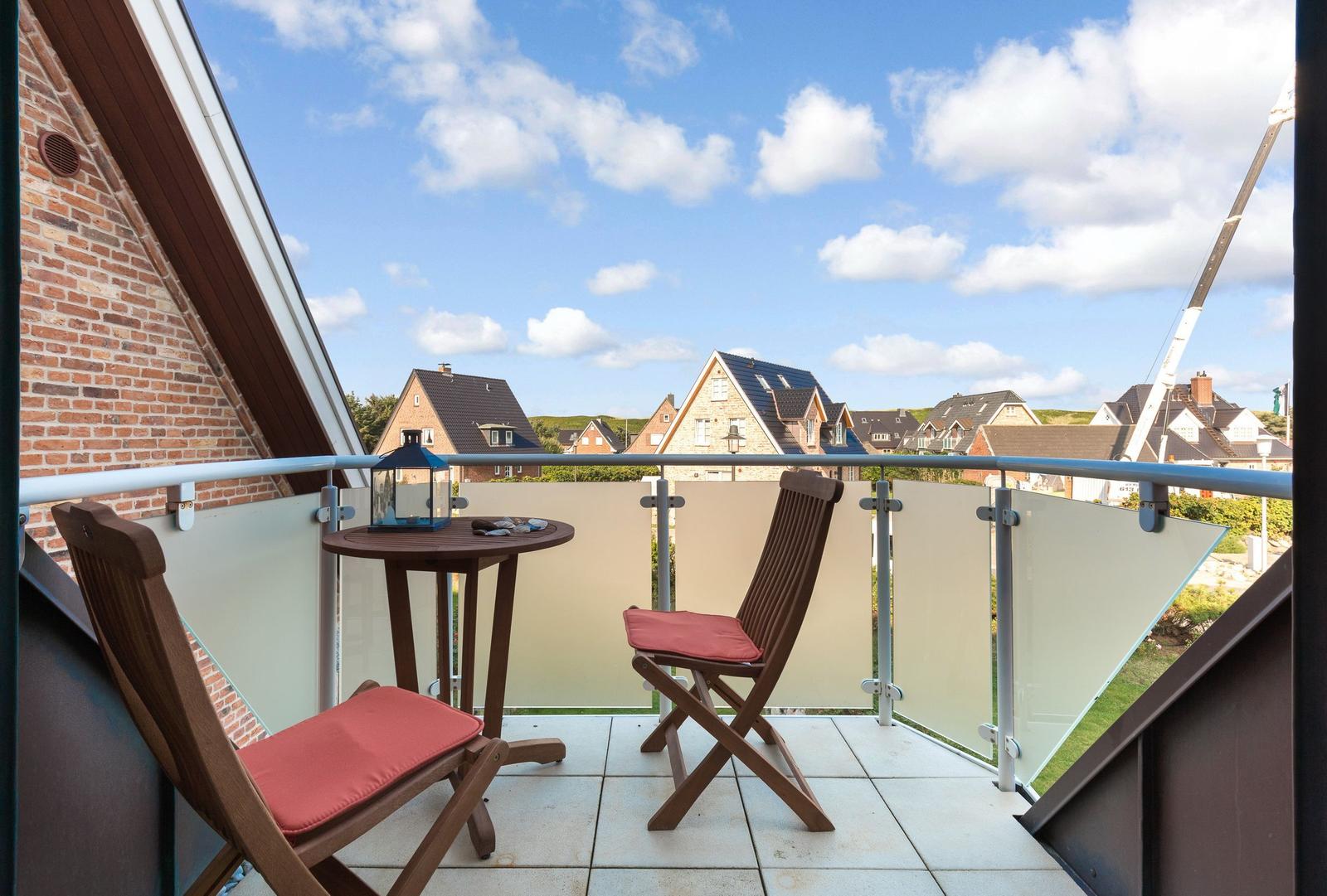 Balcony with two wooden chairs and a table. View of houses and sky.