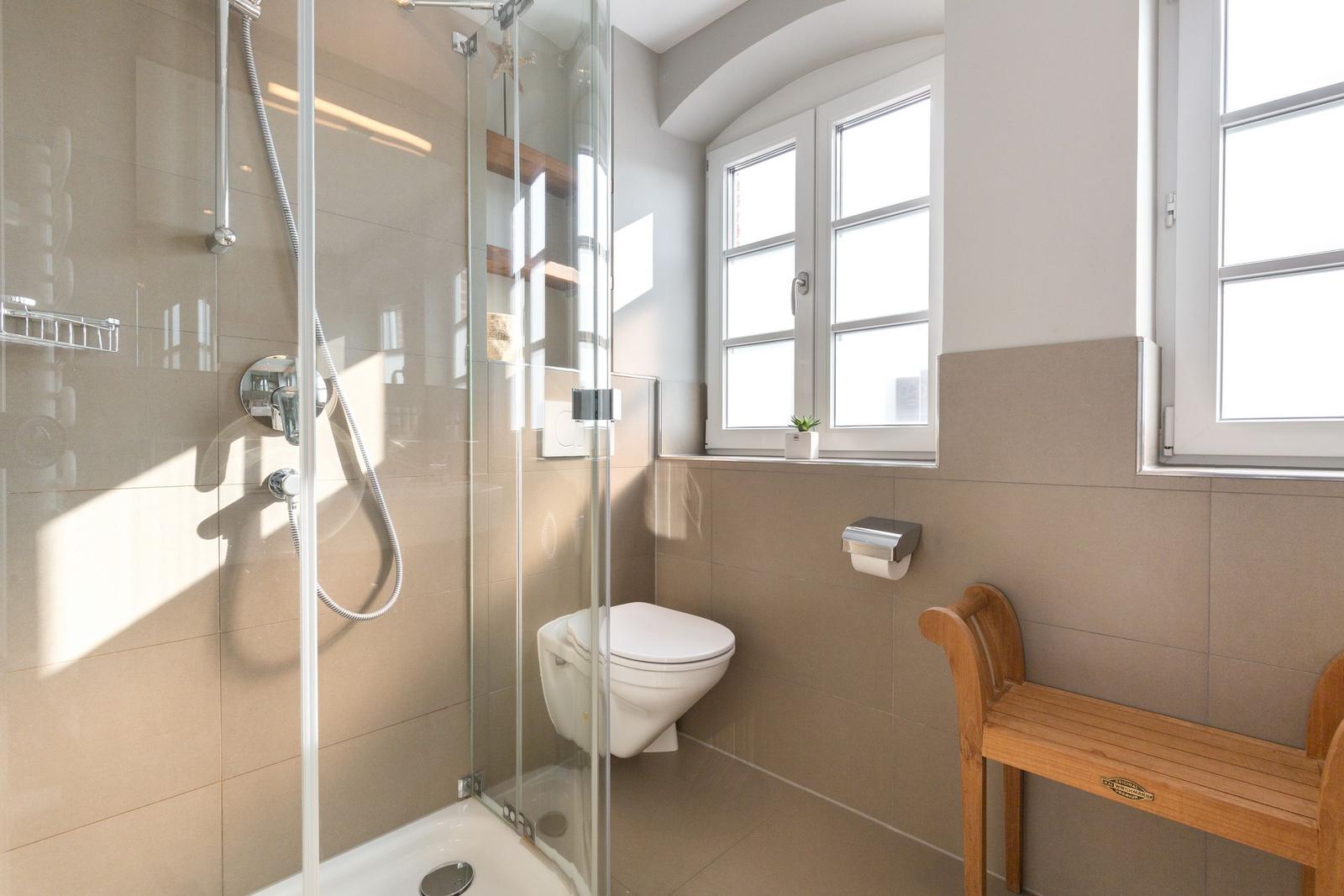 Bad mit Dusche, Toilette und Holzbank. Fenster mit Pflanze.