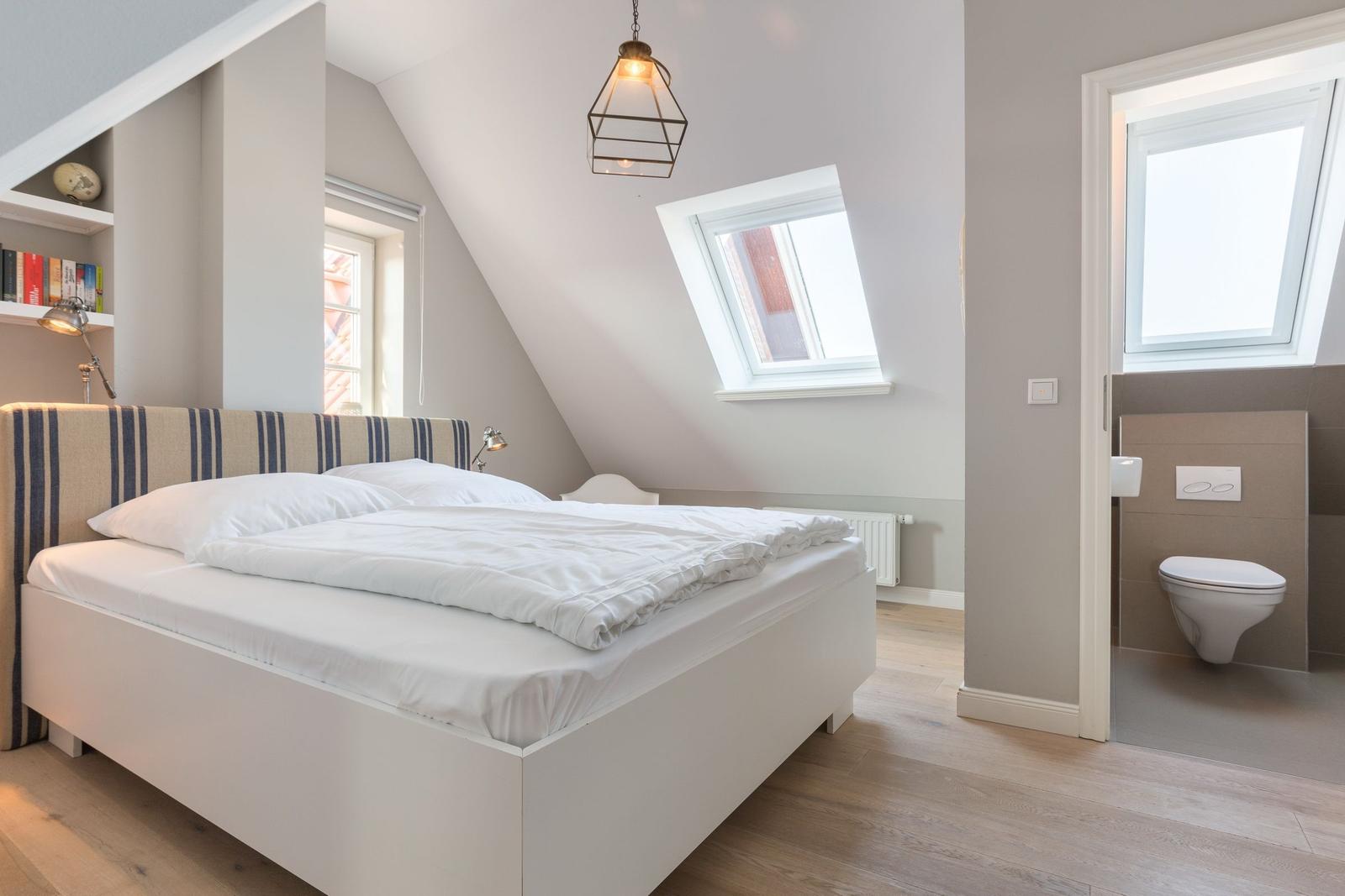 Schlafzimmer mit Dachschräge, Doppelschreibtisch und Fenster. Nebenraum mit Toilette und Dachfenster.