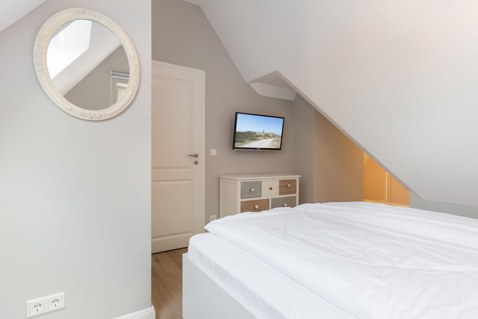 Schlafzimmer mit Dachschrägen, Bett, TV und Spiegel an der Wand.