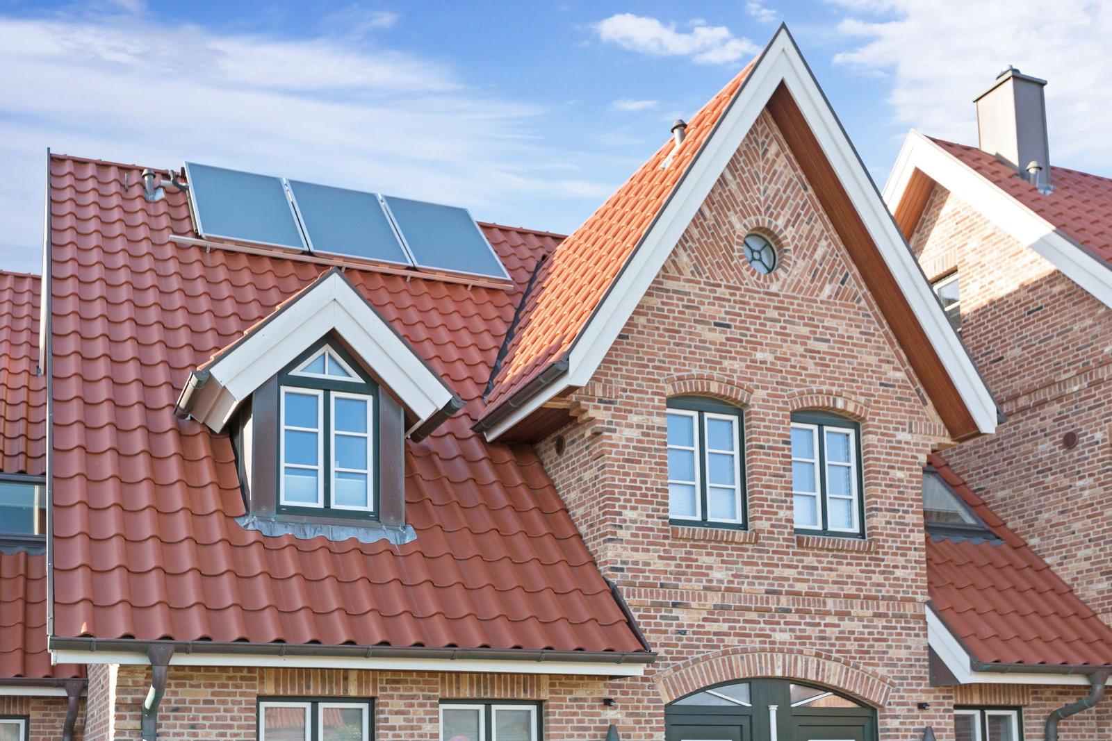 Rotes Ziegeldach mit Solaranlage und Dachfenster an einem Backsteinhaus.