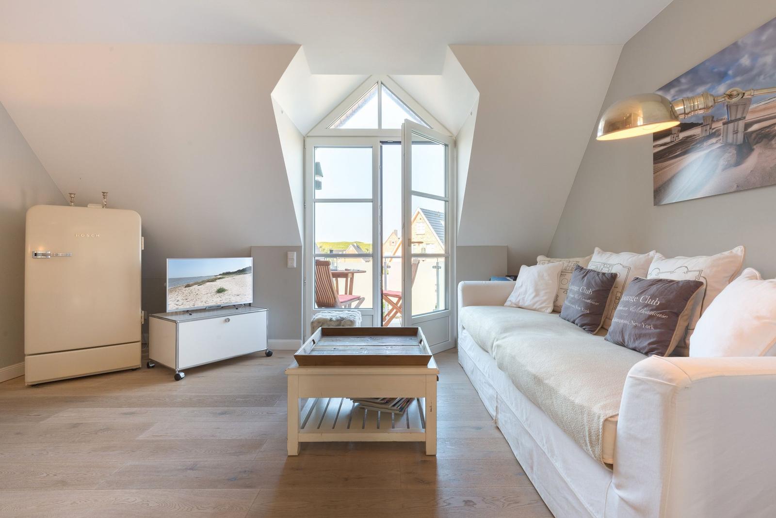 Wohnzimmer mit Sofa, Kühlschrank und Balkontür.