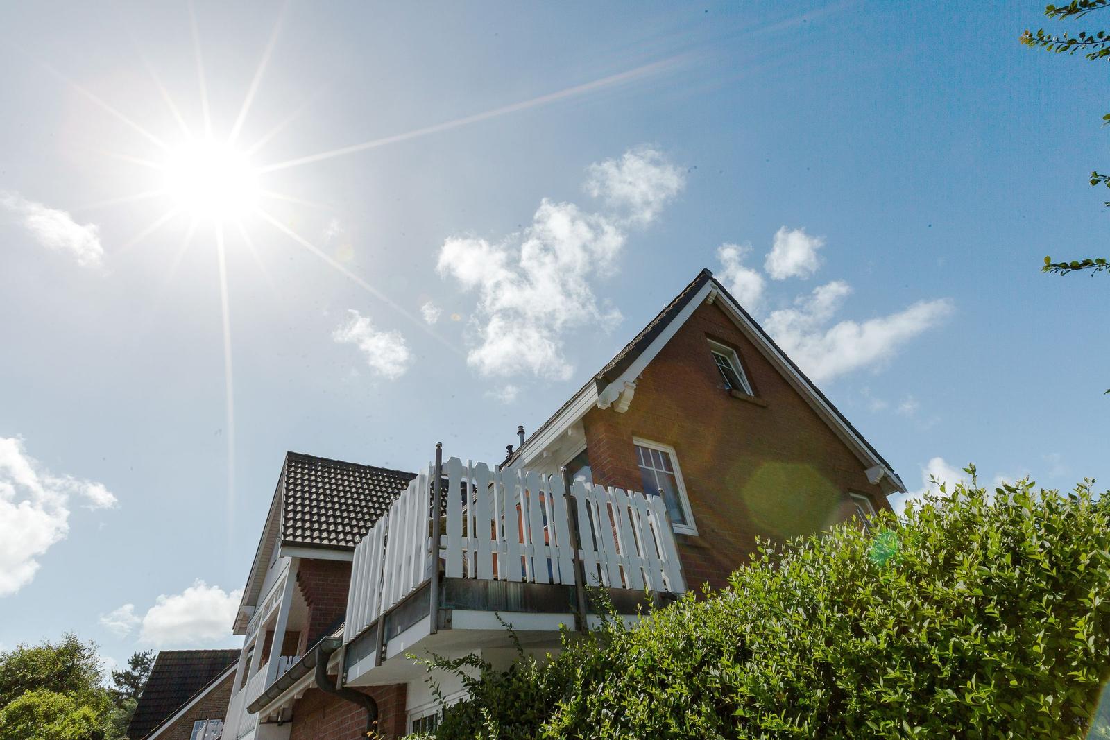 House with balcony under bright sunlight and blue sky with white clouds.
