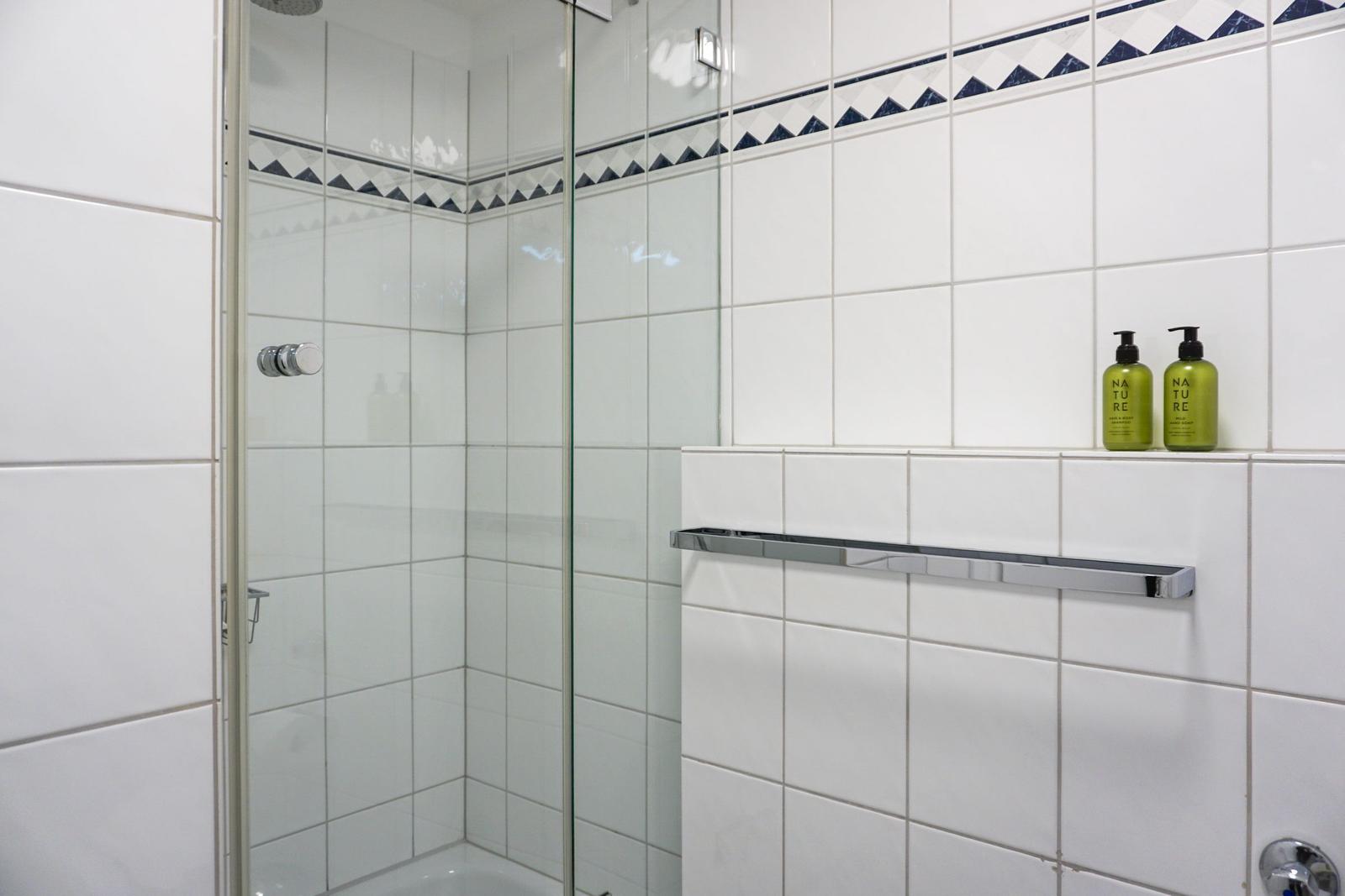 Shower cabin with glass door and white tiles. Two green bottles on the wall.
