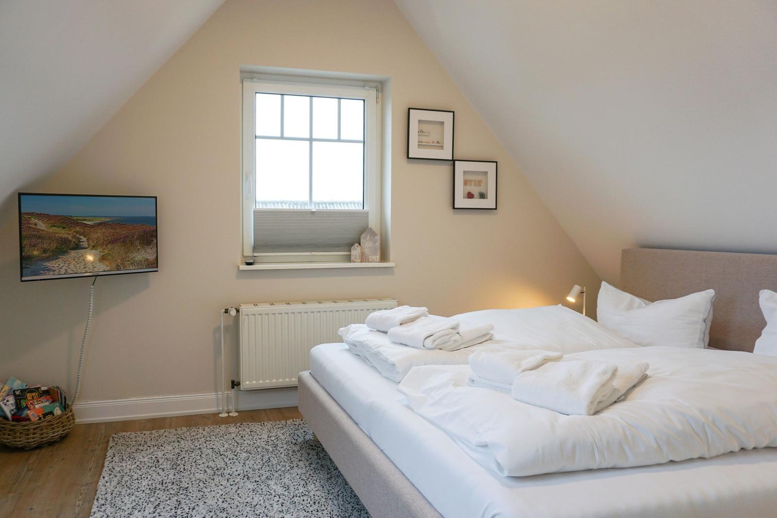 Bedroom with sloped ceiling, bed, window, and wall art.
