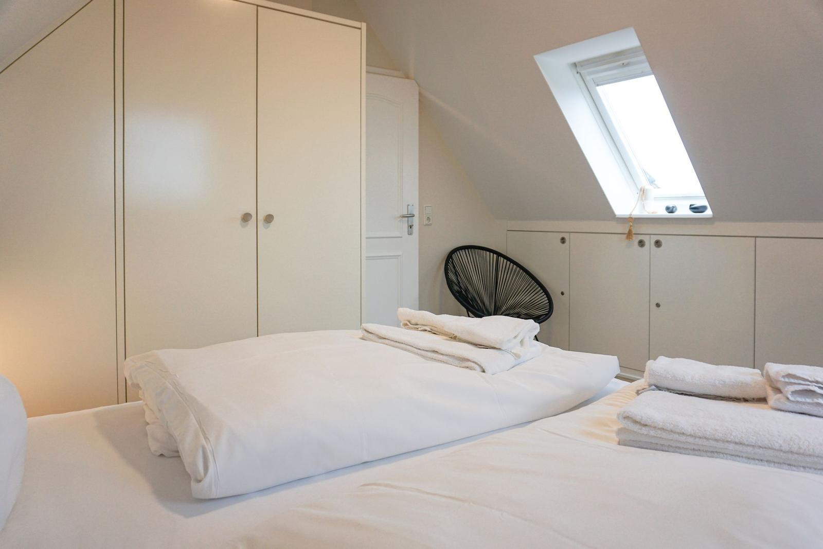 Bedroom with sloped ceiling, skylight, and white bed.