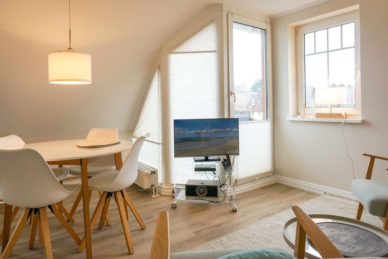 Living and dining area with TV, table and chairs, and windows.