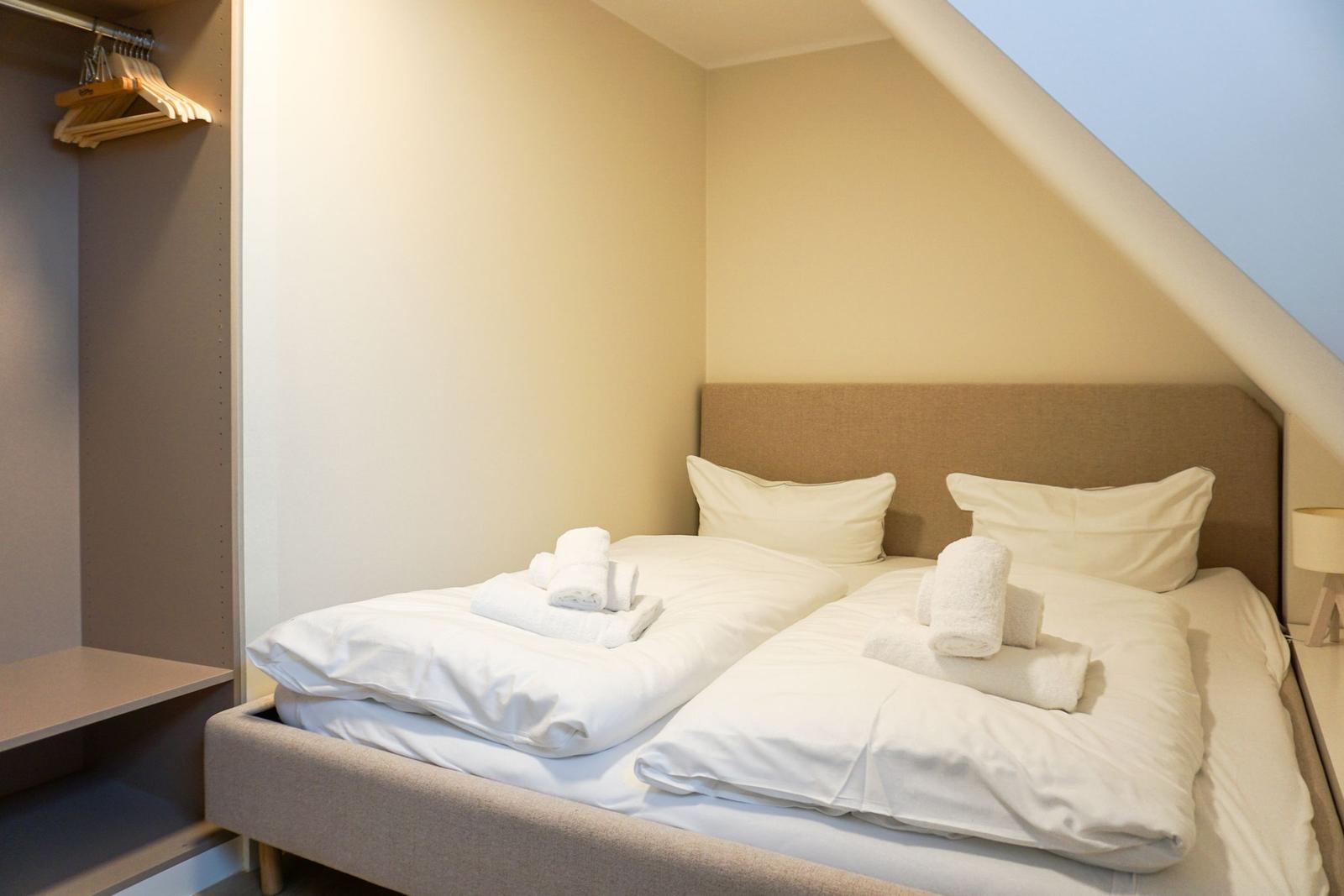 Bedroom with double bed, pillows, and folded towels under sloped ceiling.