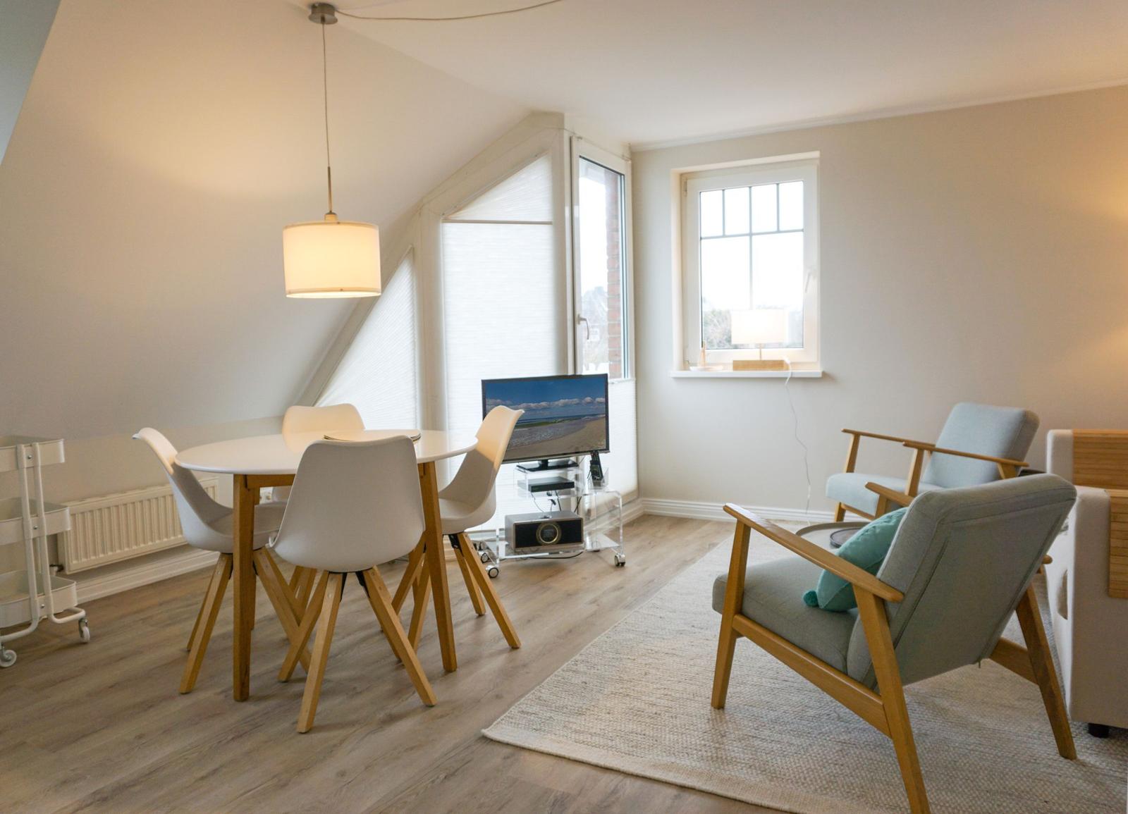 Dining area with table, chairs, and TV. Two armchairs on rug.