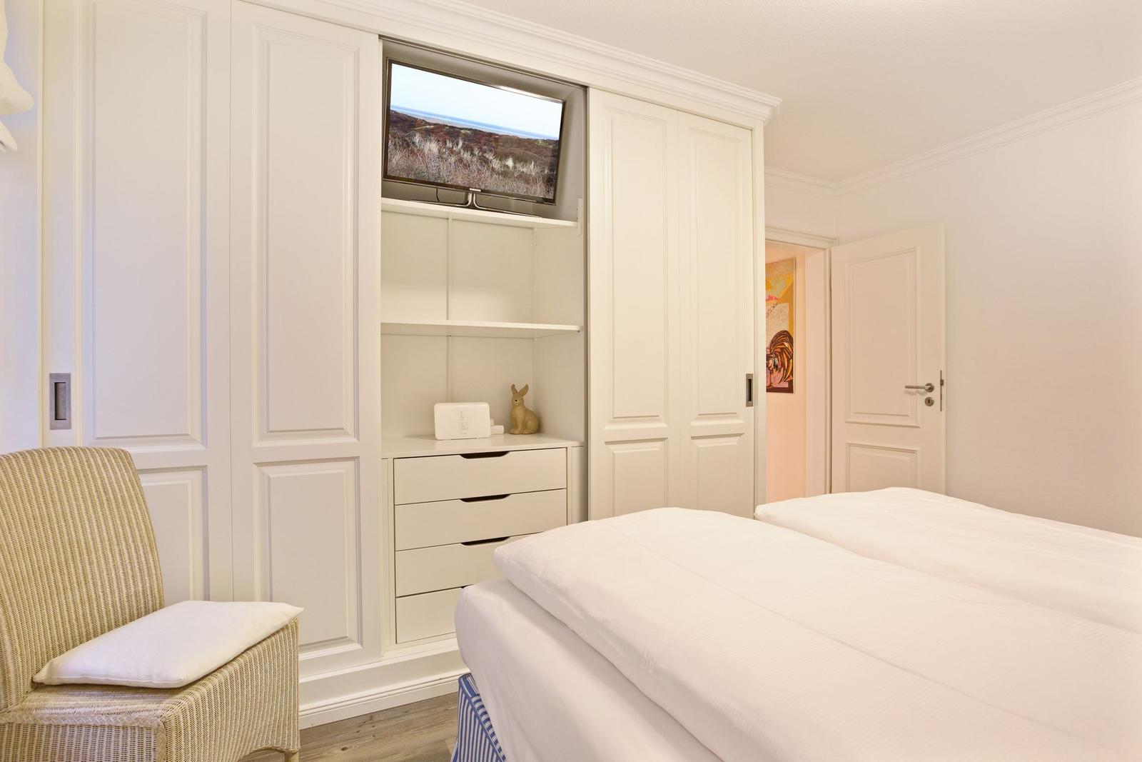 Schlafzimmer mit weißem Bett, Kleiderschrank und Fernseher.