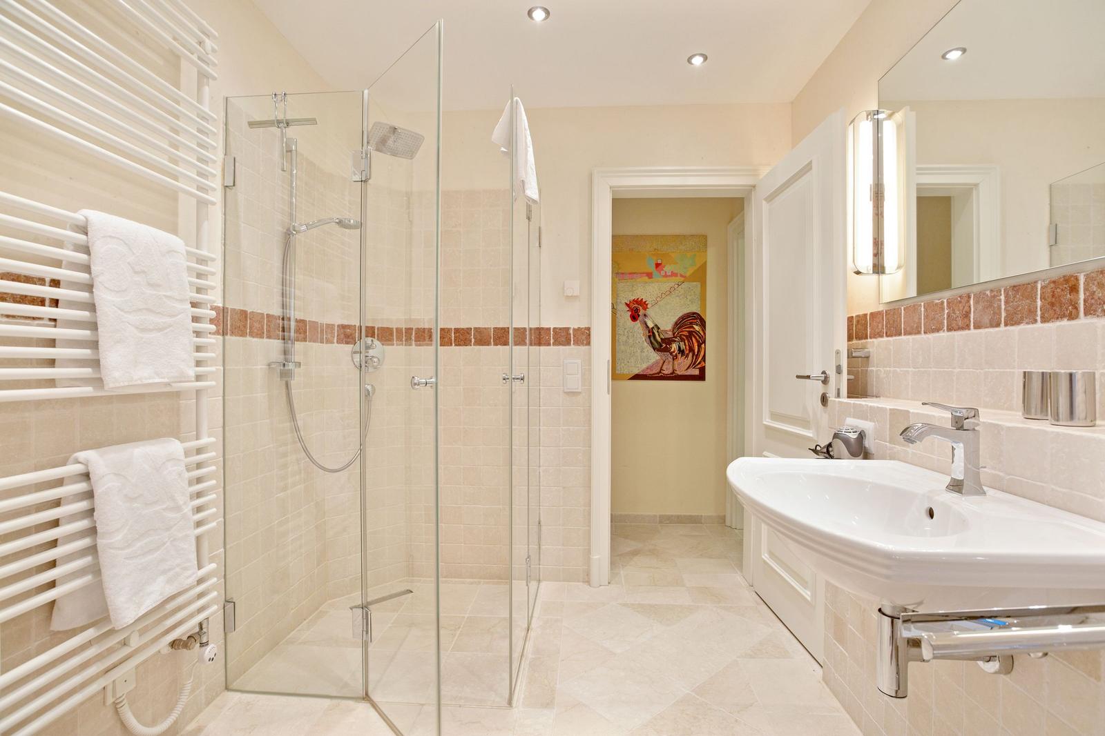 Badezimmer mit Dusche, Waschbecken und Heizkörper mit Handtüchern.
