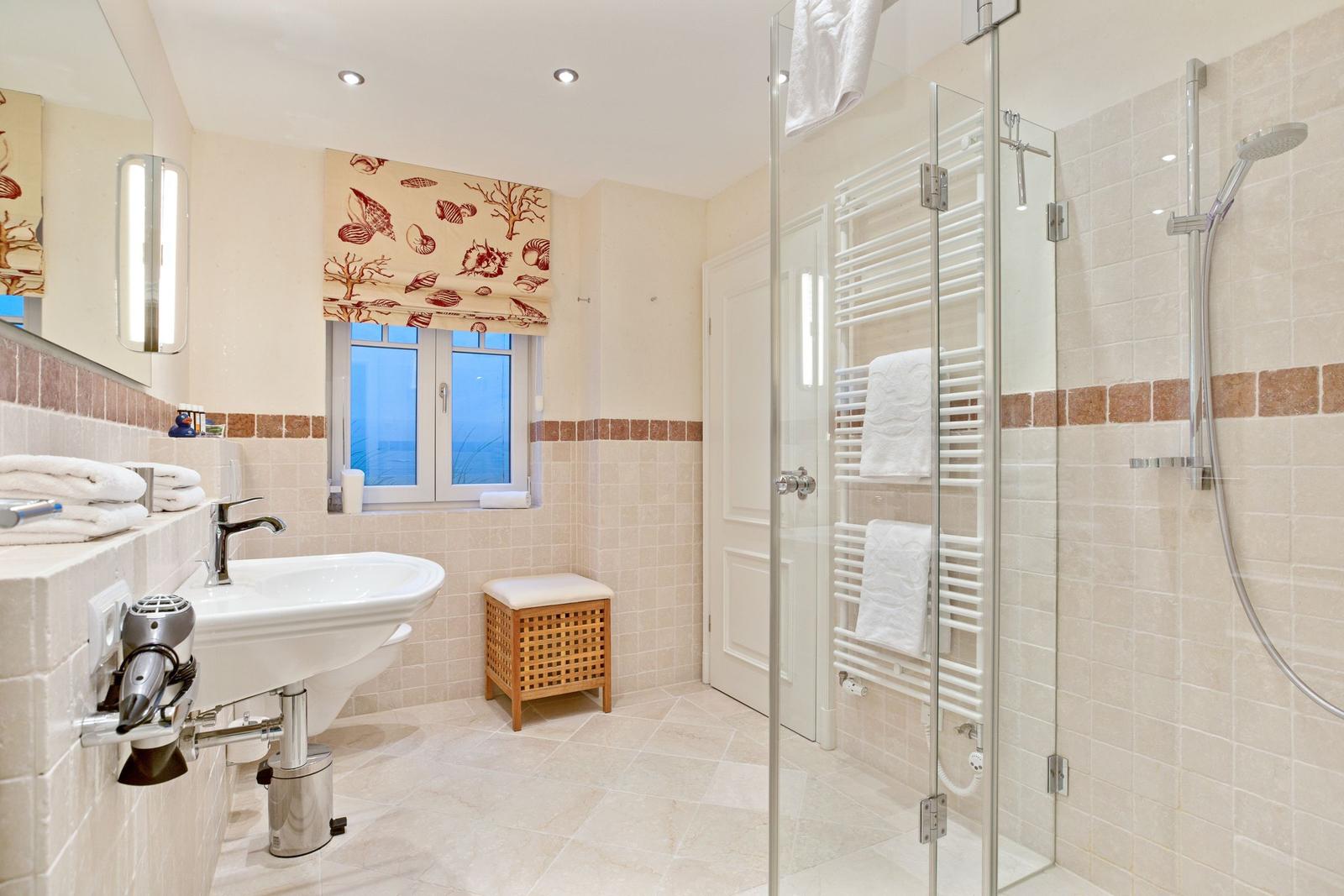 Badezimmer mit Dusche, Waschbecken und Fenster mit Meerblick.
