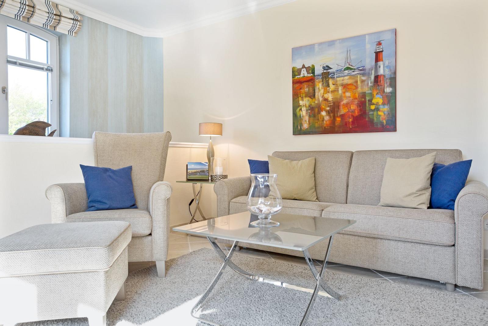 Wohnzimmer mit Sofa, Sessel und Glas-Tisch. Wandbild zeigt Leuchtturm.