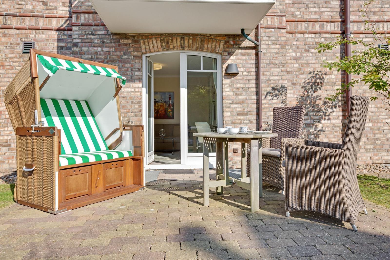 Terrasse mit Strandkorb, Tisch und Stühlen vor einer Glasfront.