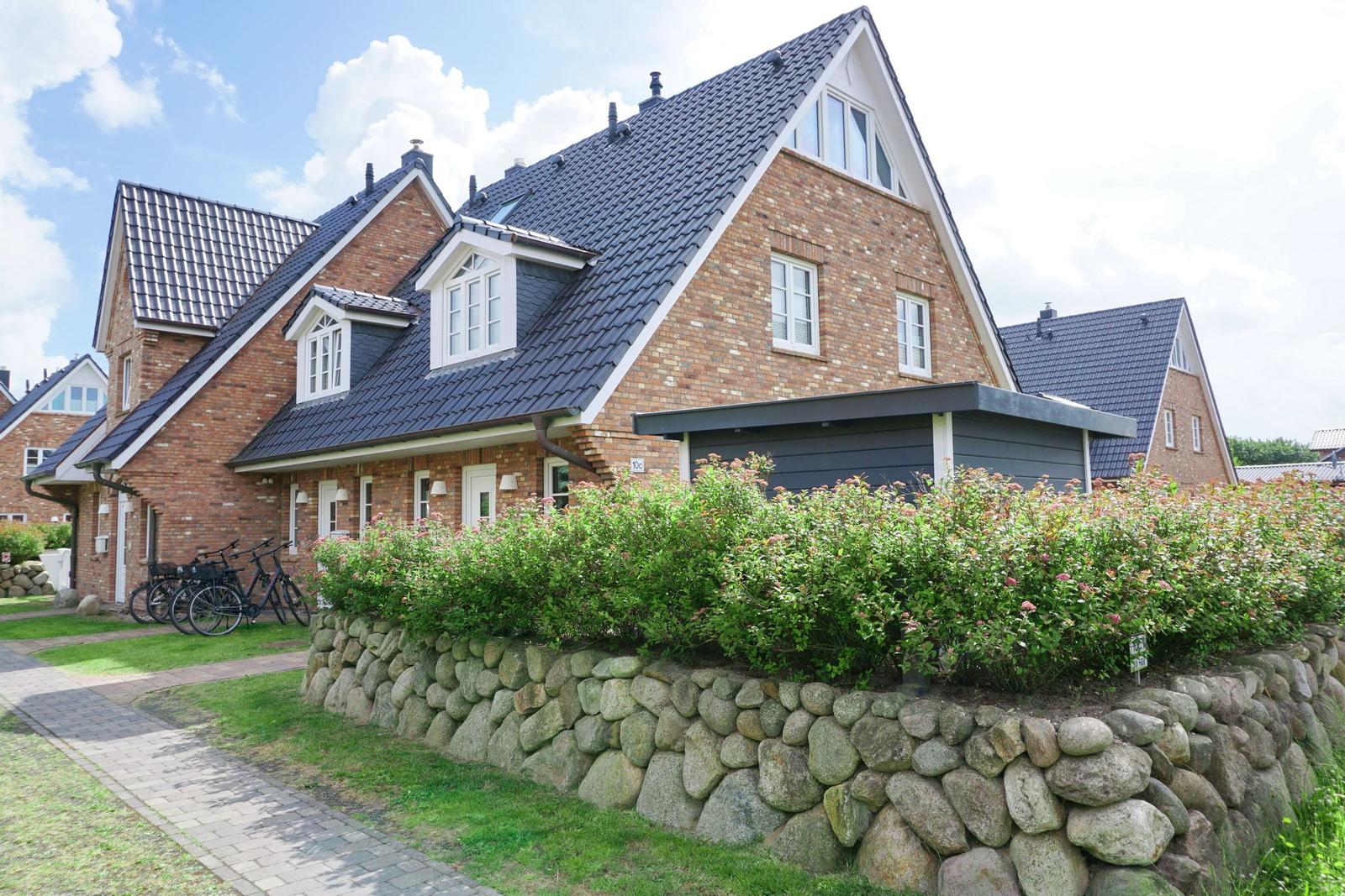 House with brick facade, dark roof, and stone wall with berry bushes.