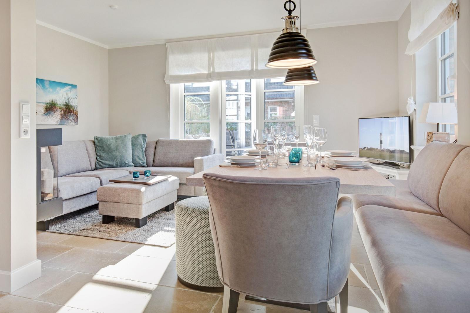 Living and dining area with sofa, table, and chairs. Windows and ceiling lights visible.