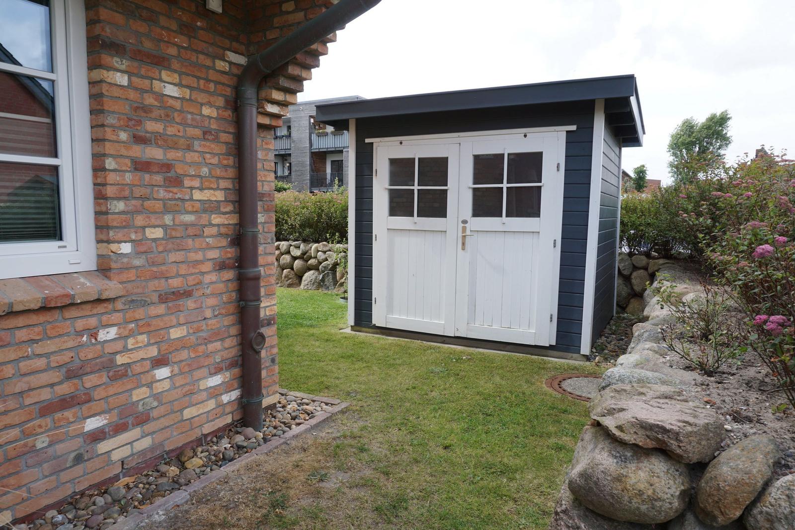 Behind the house is a small shed with white doors and dark siding.