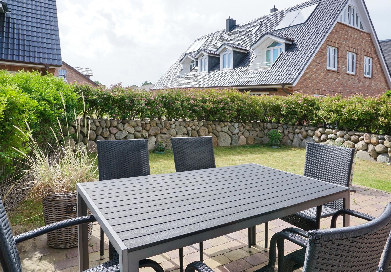 Terrace with table and chairs, lawn and stone wall in background.