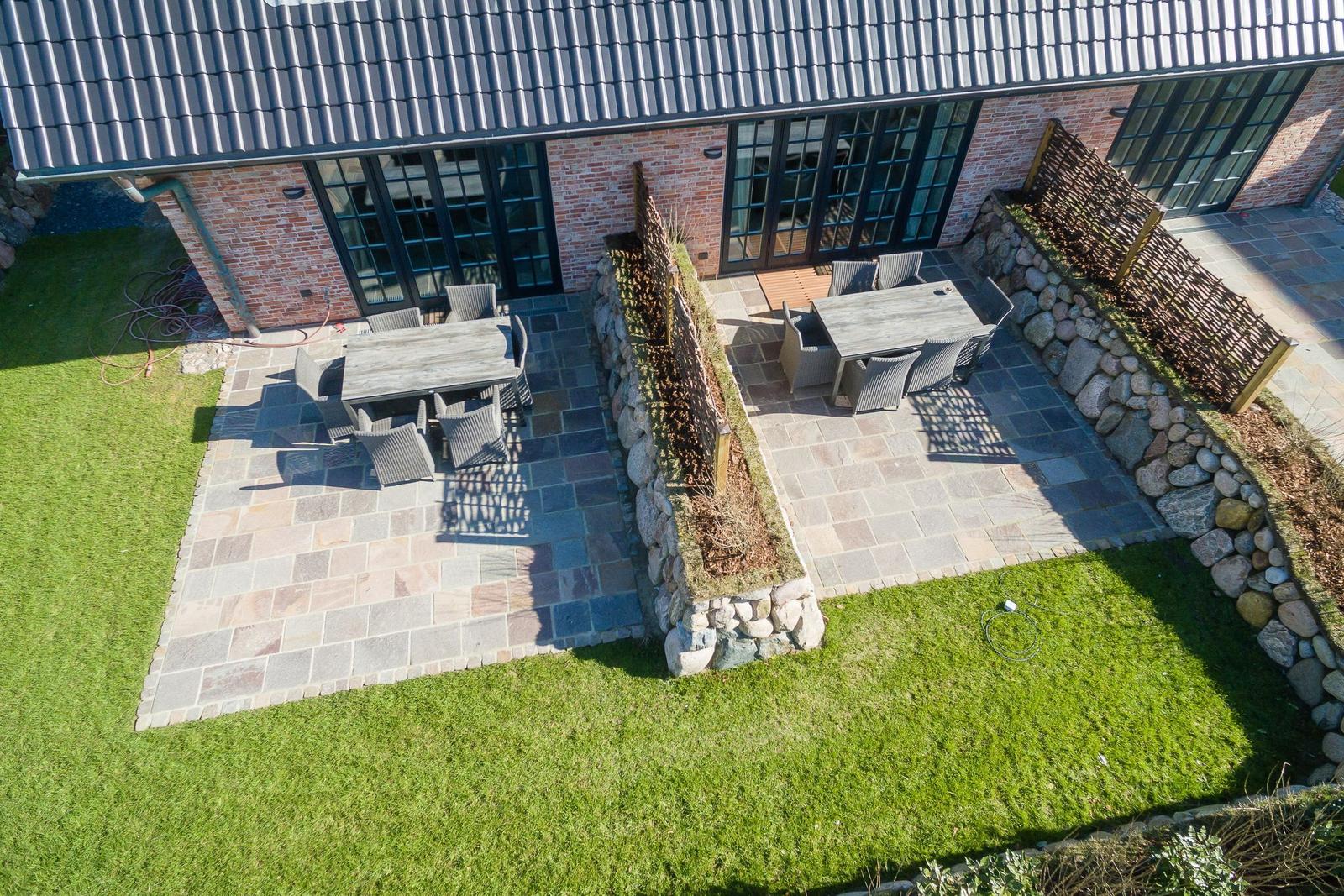 Terrasse mit Tischen und Stühlen, umgeben von Steinmauern und Rasen.