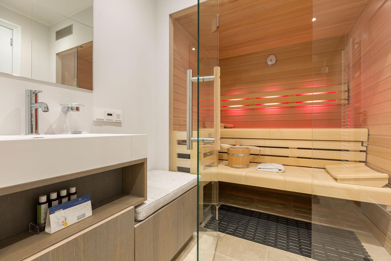 Sauna mit Holzbank und Glaswand. Neben dem Waschbecken mit Spiegel.