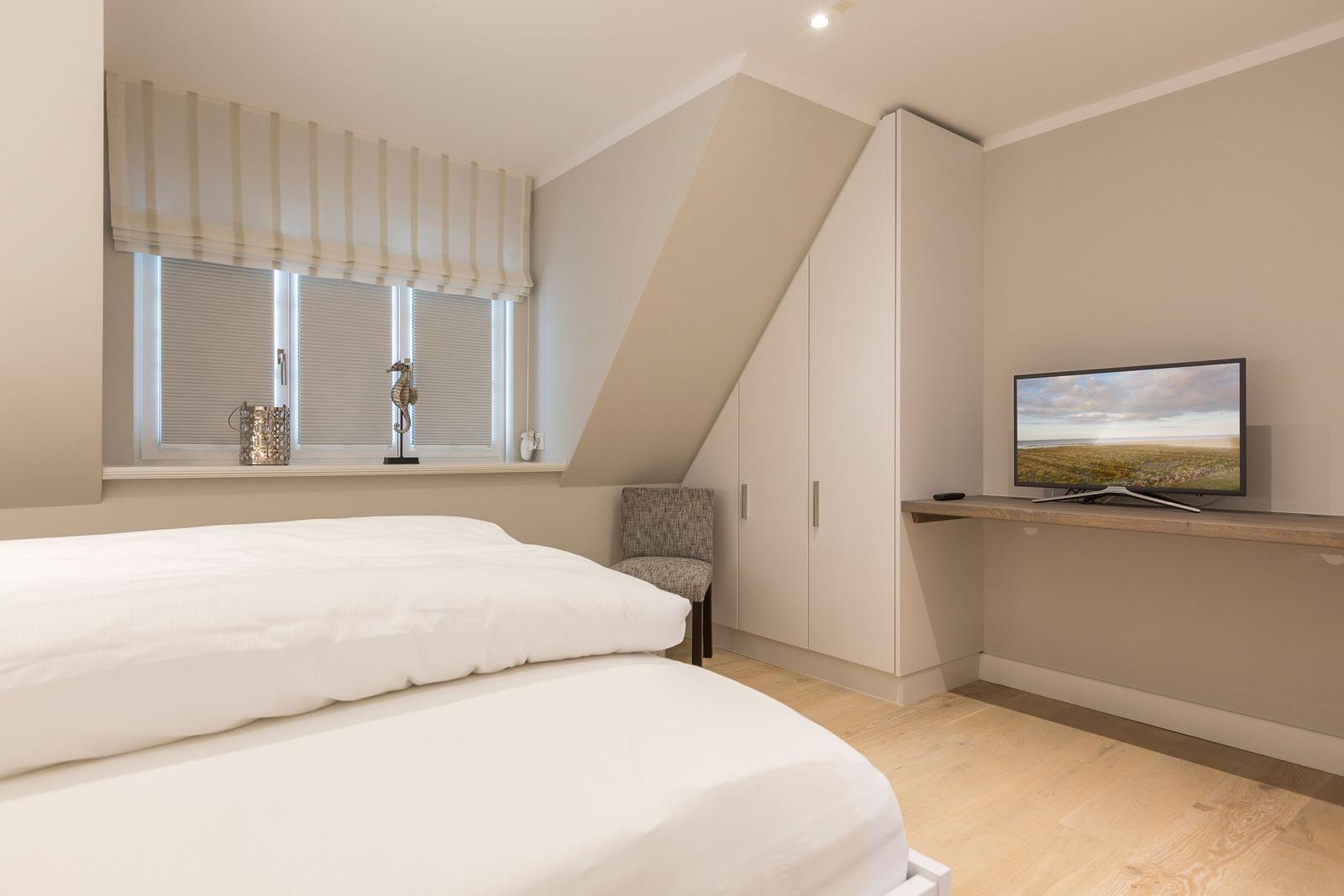 Schlafzimmer mit Dachschräge, Bett, Schrank und TV.