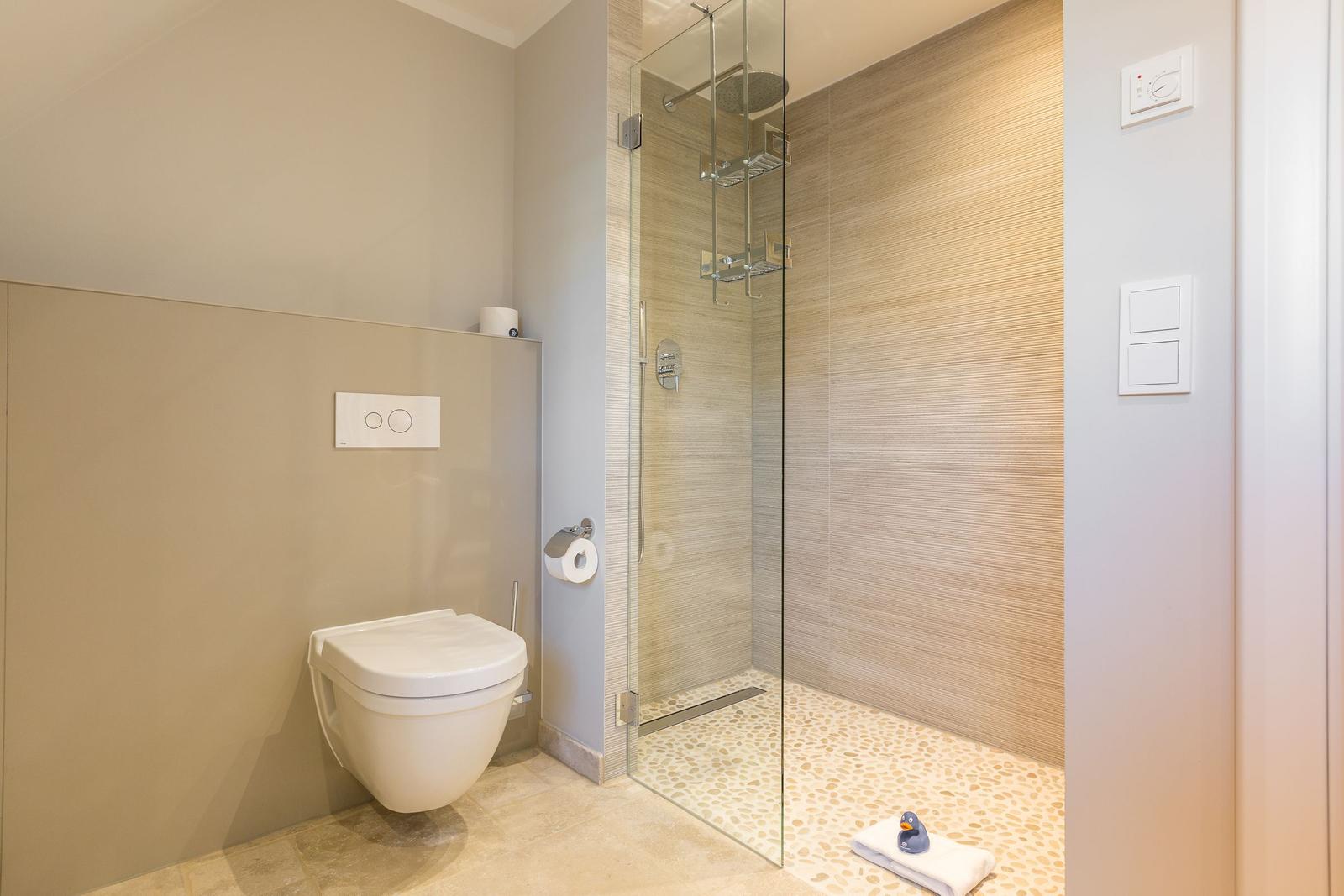 Dusche mit Glaswand, Toilette und Handtuch auf Steinboden.