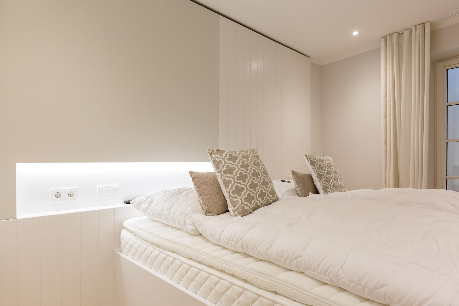 Schlafzimmer mit Bett, Kissen und Vorhängen an Fenster.
