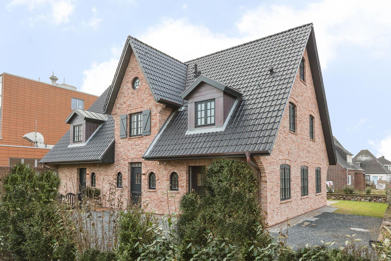 Rotes Backsteinhaus mit dunklem Satteldach und grünen Hecken.