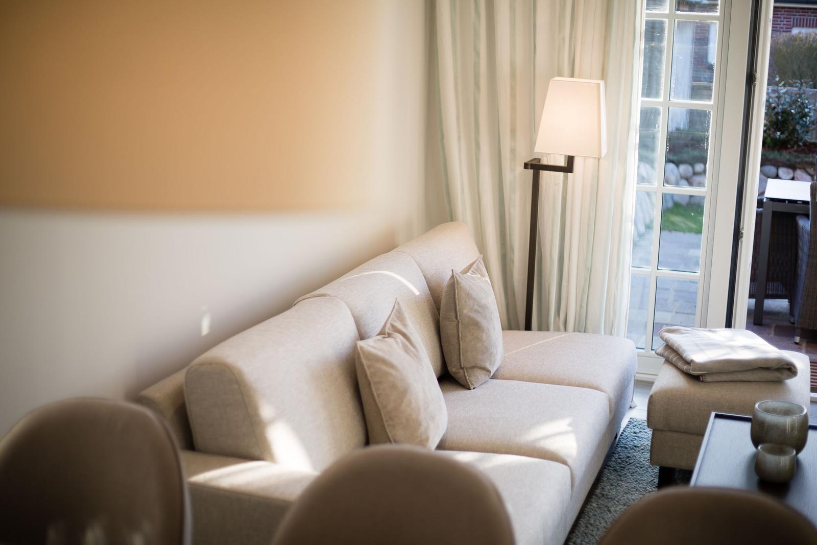 Ein Sofa mit Kissen steht vor einer Glastür. Daneben steht eine Stehlampe.