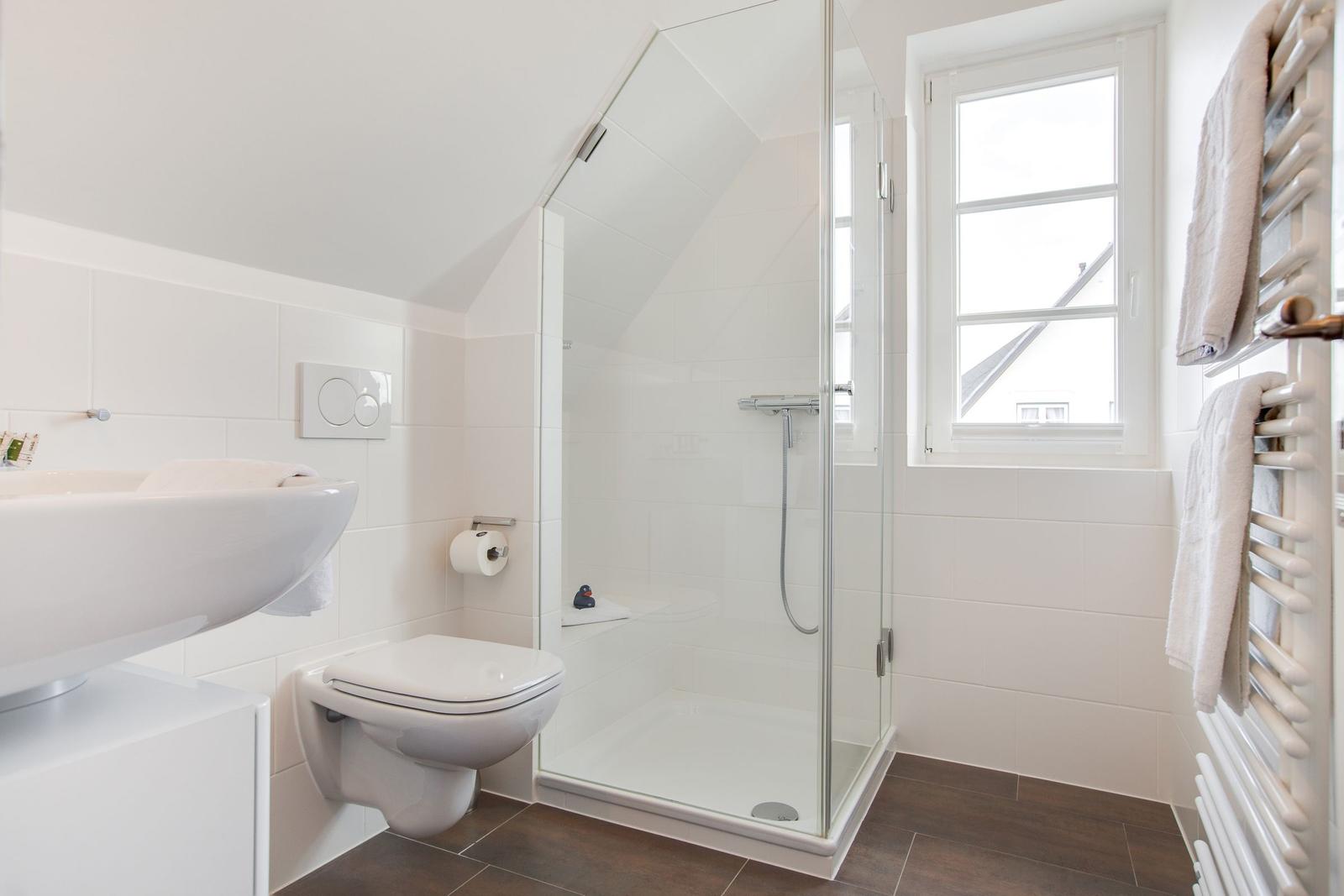 Bathroom with shower, toilet, and sink. Window and towel rack visible.