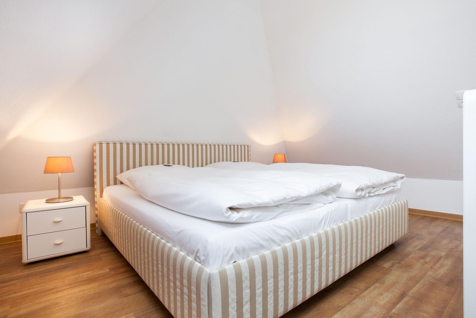 Bedroom with bed, nightstand, and lamp. Wooden floor and sloped ceiling.