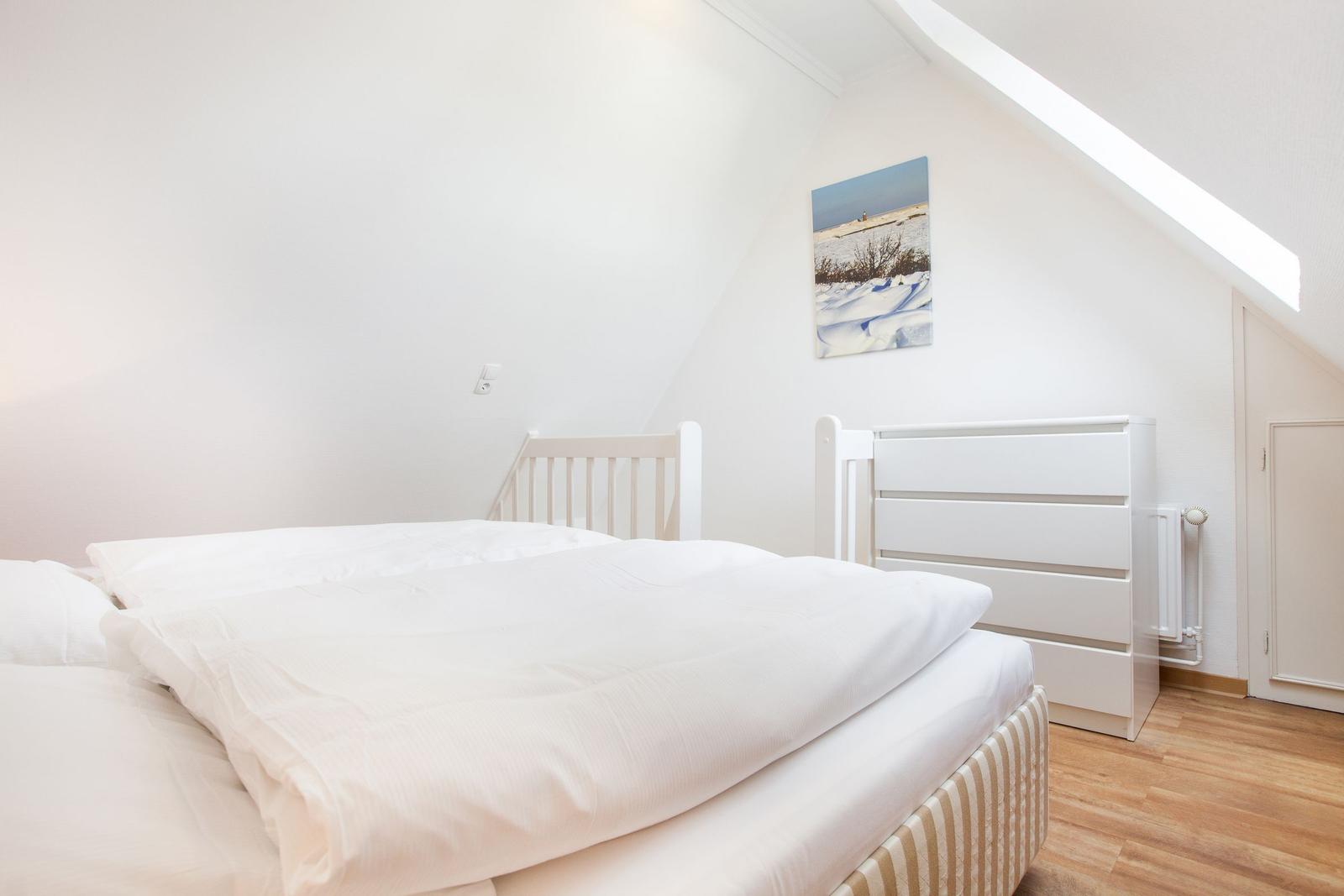Bedroom with white bed, wooden floor, and sloped ceiling.