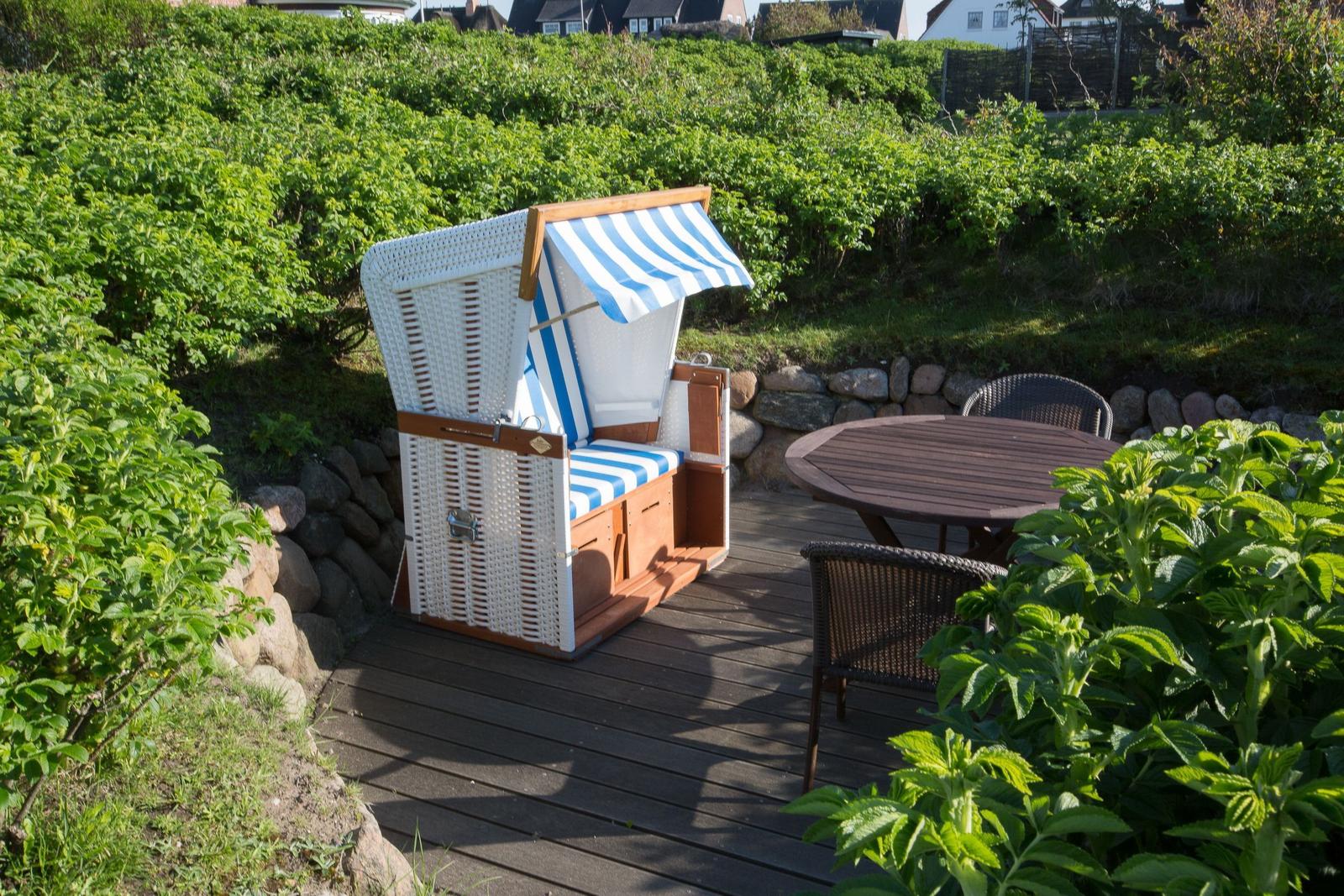 Deck with beach chair, table and chairs surrounded by greenery.
