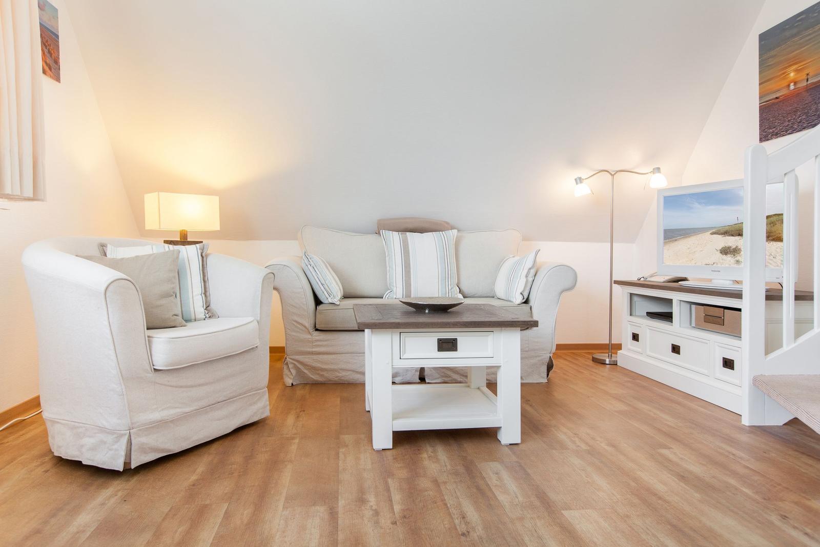 Living room with sofa, armchair, coffee table, and TV on wooden floor.