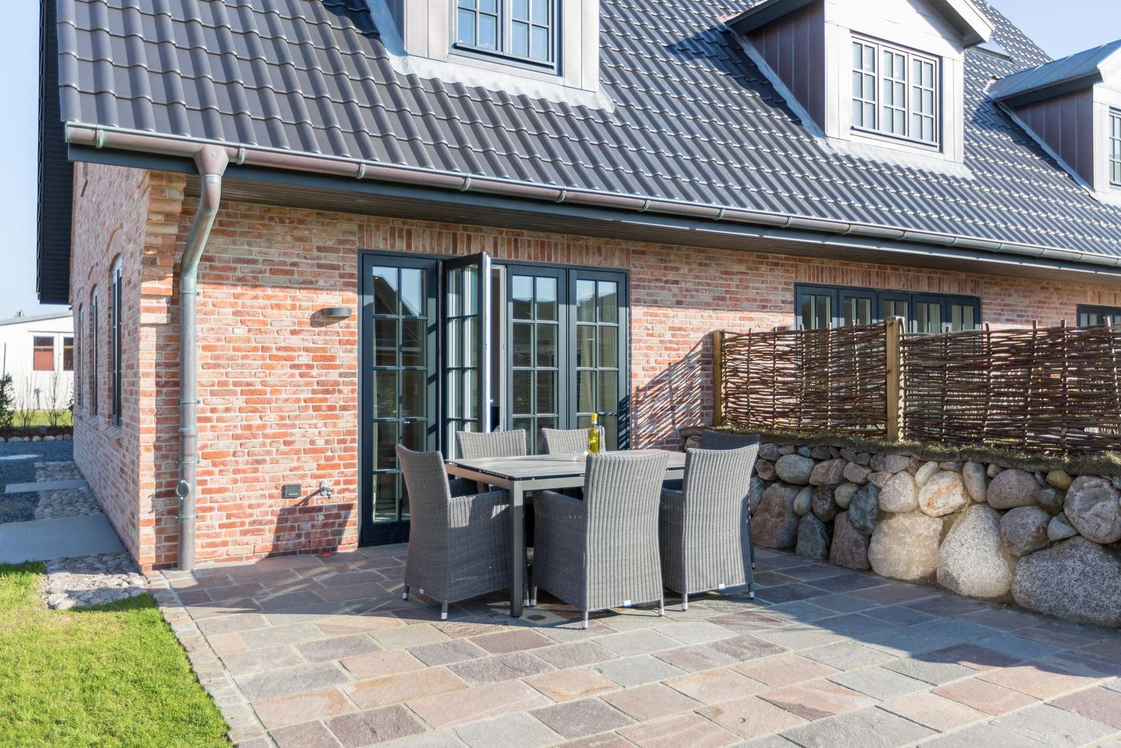 Terrace with table and chairs in front of a brick house with dormers.